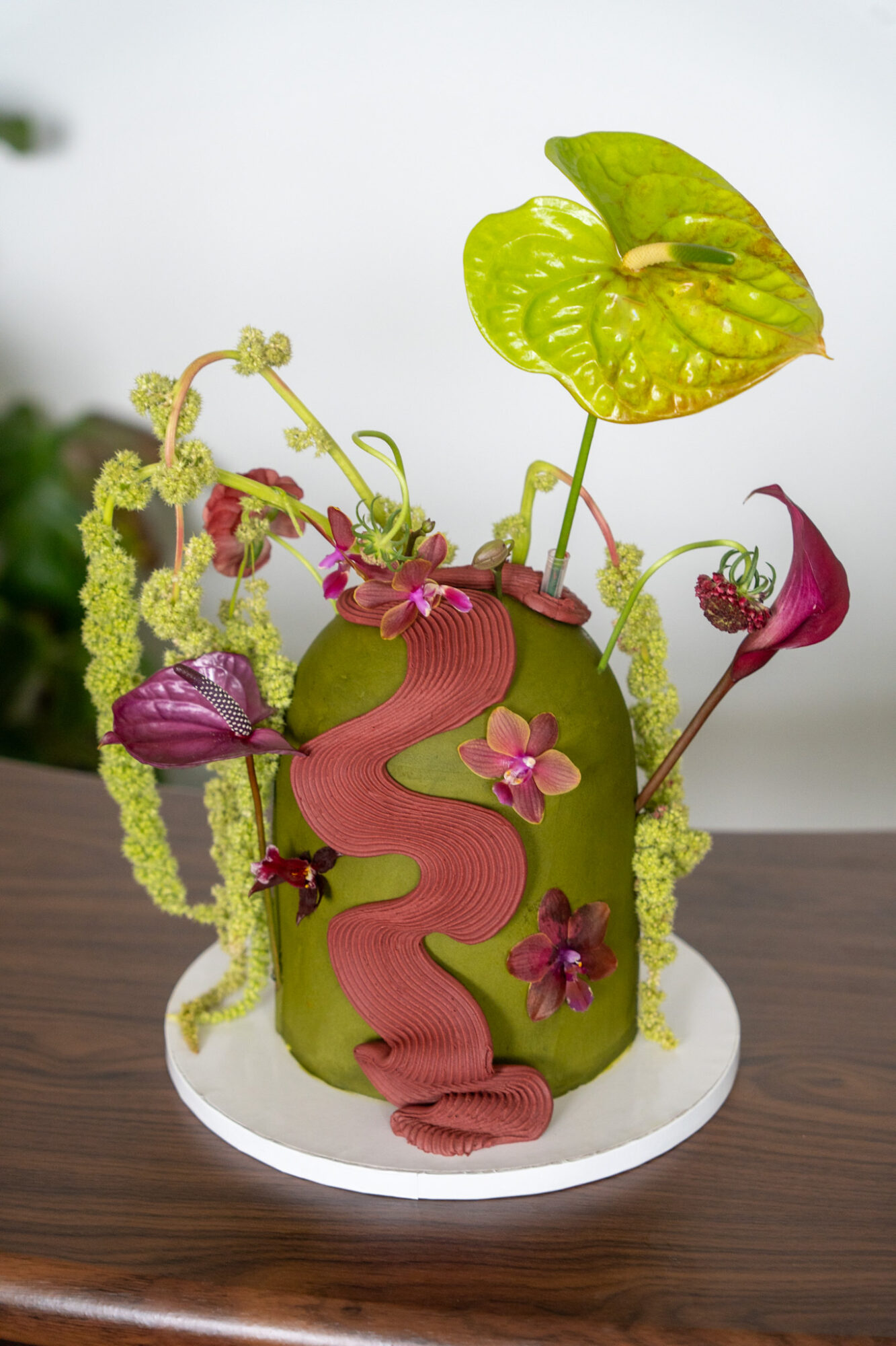Cake decorated with green leaves, pink flowers, and a pink ribbon, resembling a plant or nature theme.