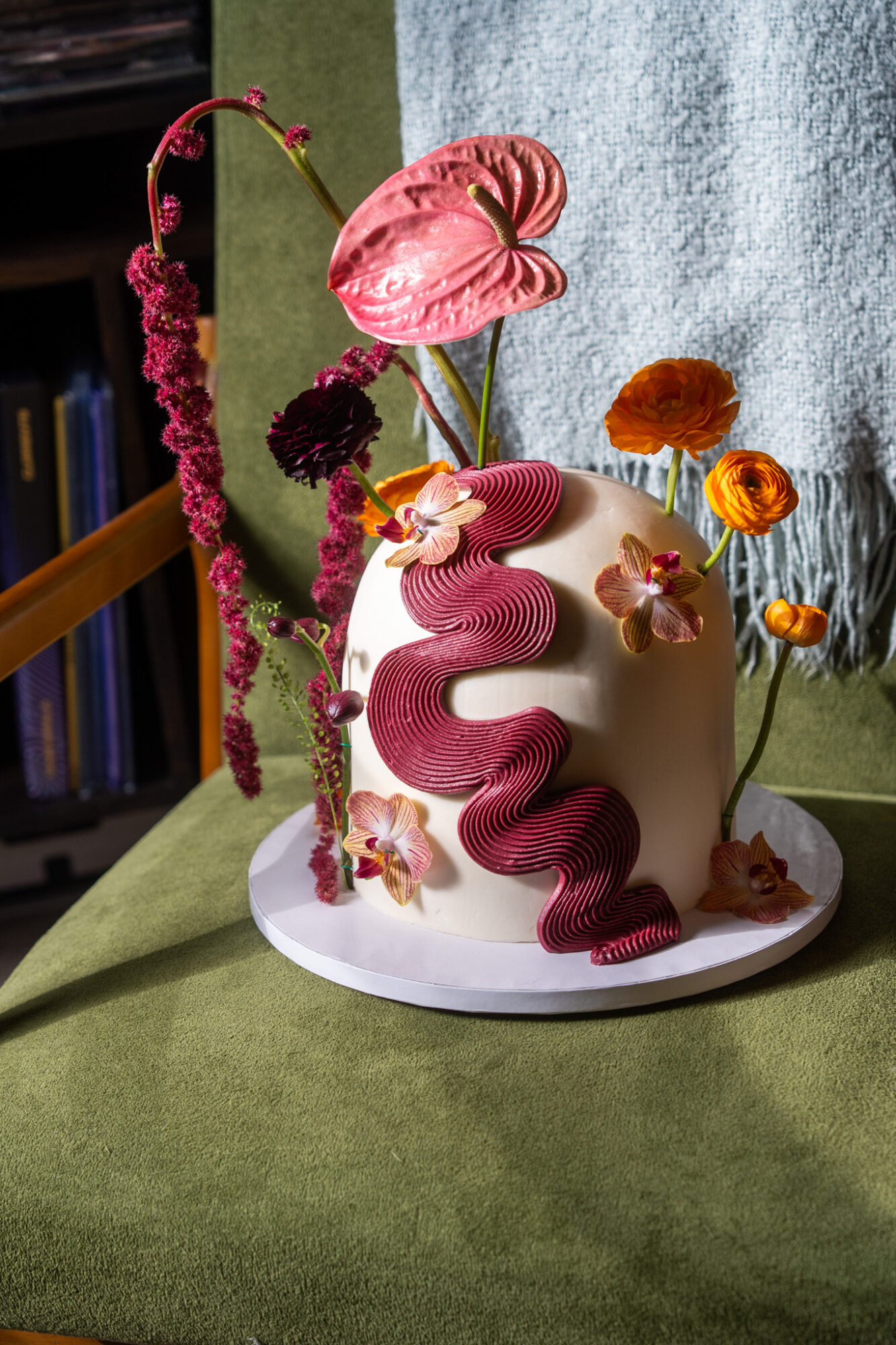 Decorative cake with pink snake, flowers, and a pink mushroom on top, set on a table with a green cloth.