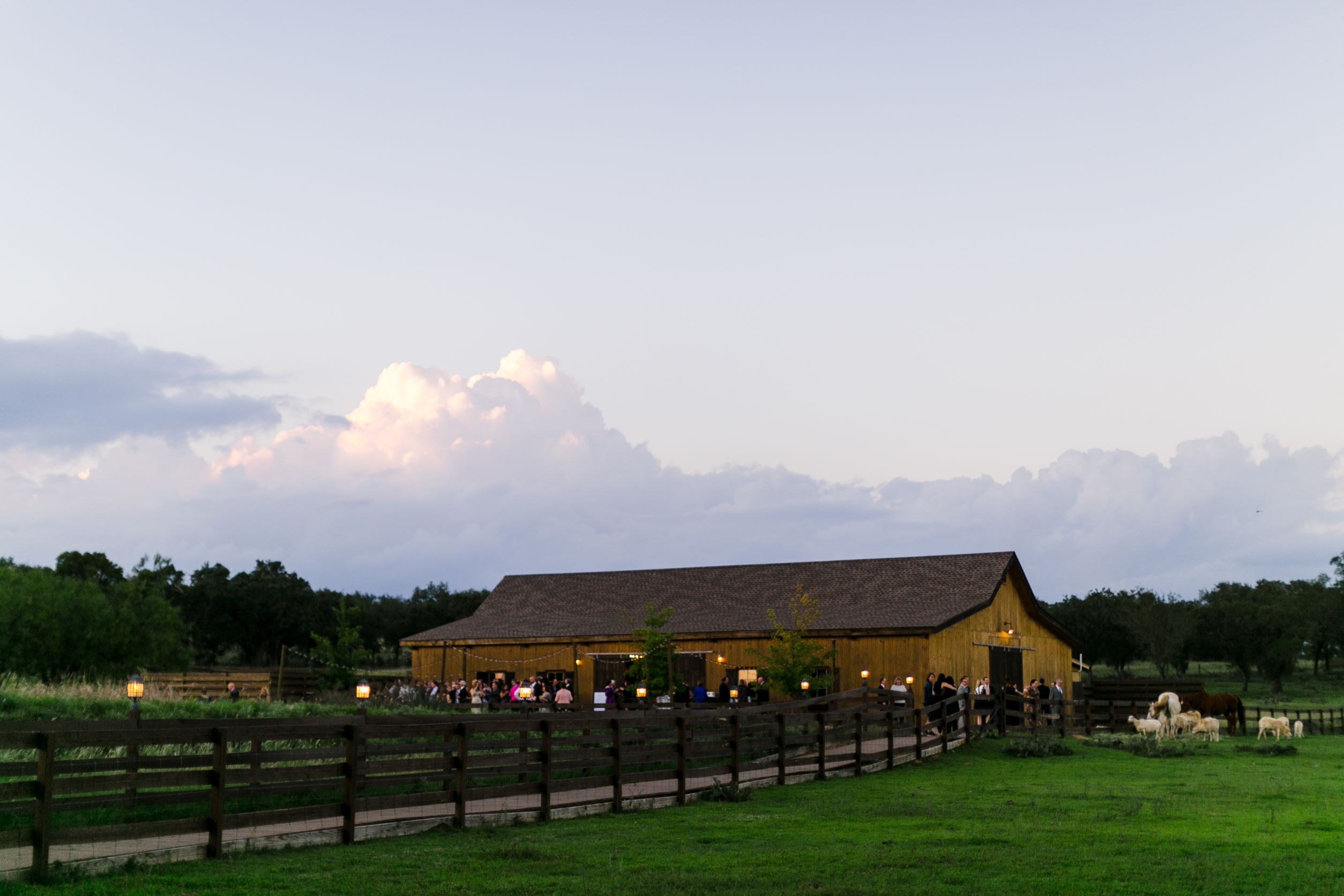 Barn with a sloped roof, surrounded by a wooden fence and green grass, under a partly cloudy sky.