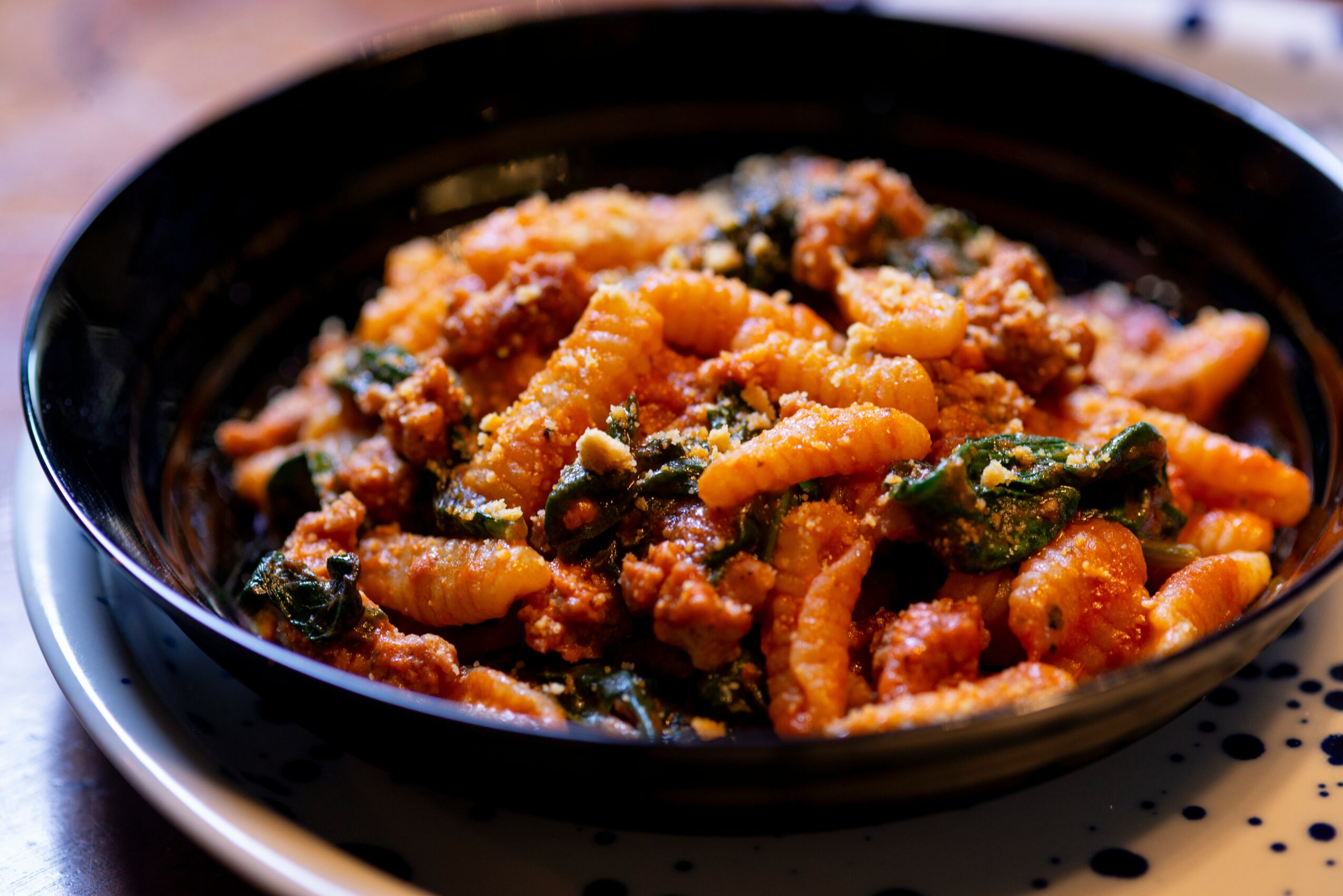 Close-up of a bowl of pasta with sauce, vegetables, and ground meat, in a black bowl on a white plate