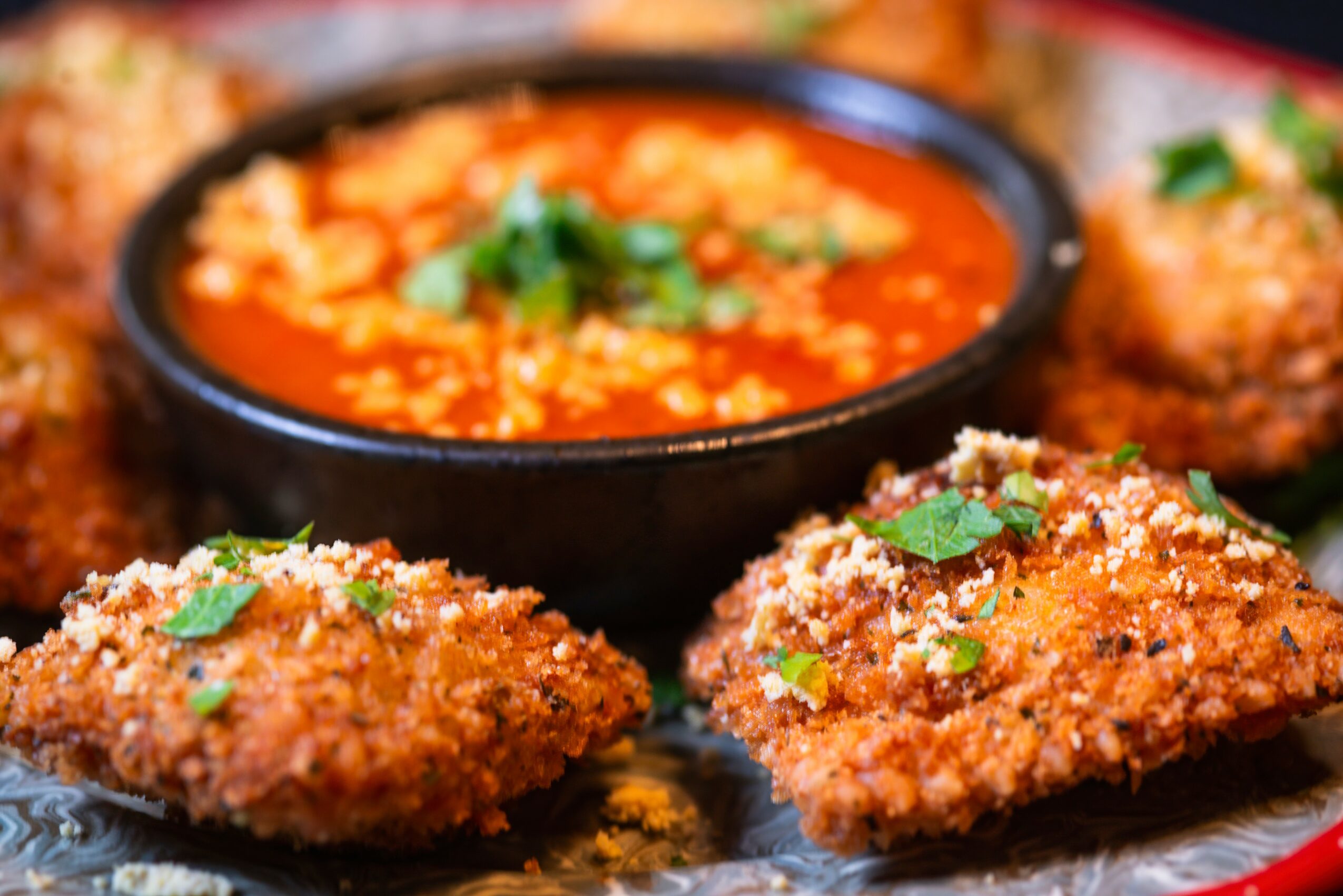 Fried food pieces with green herbs around a bowl of red sauce, on a plate.