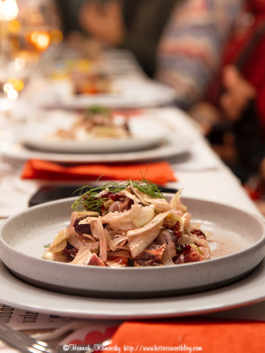 A plate of shredded meat with greens on a table, with other plates and people in the background.