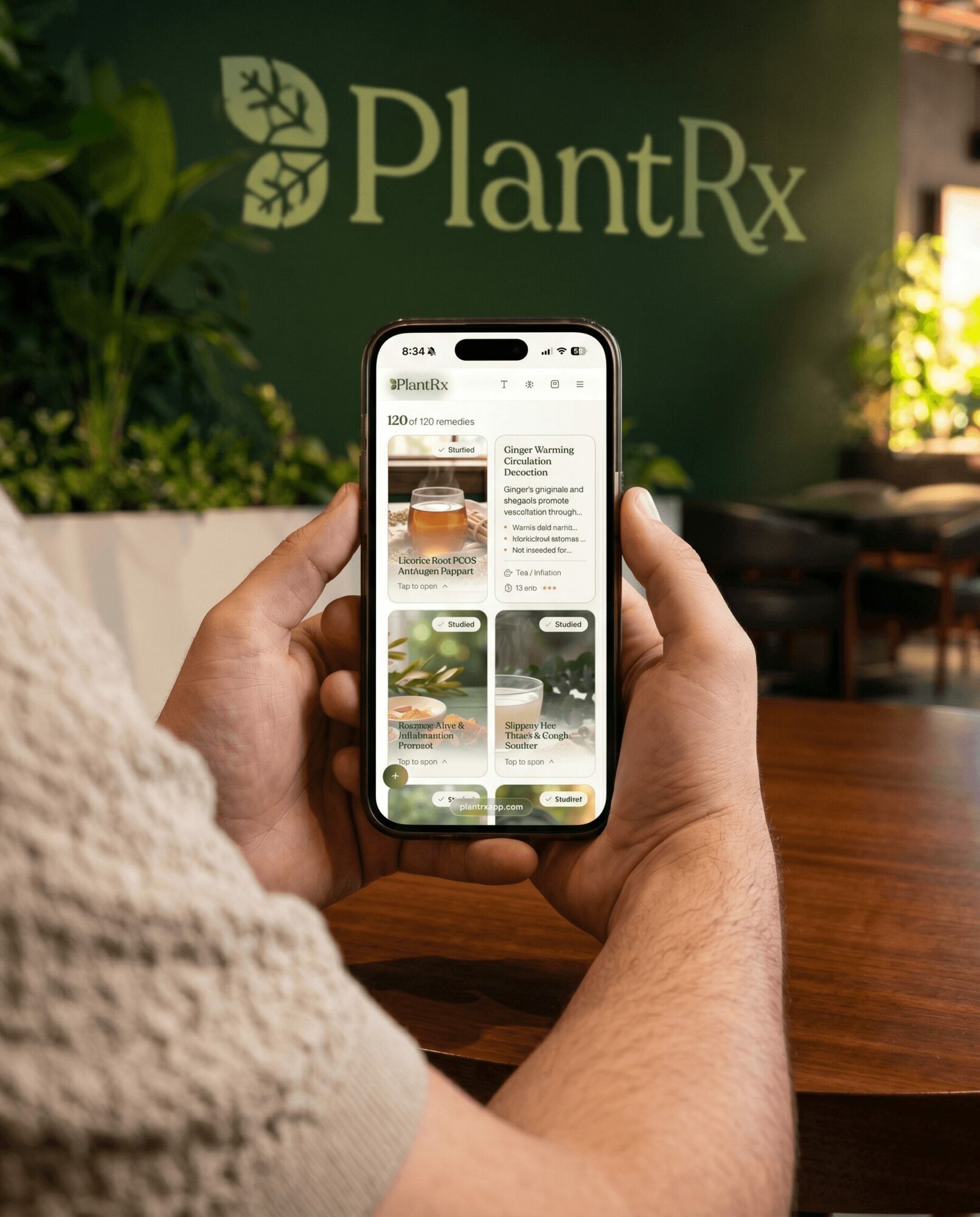 Person holding a smartphone displaying a website with plant-based products, in front of a green PlantRx sign and plants.