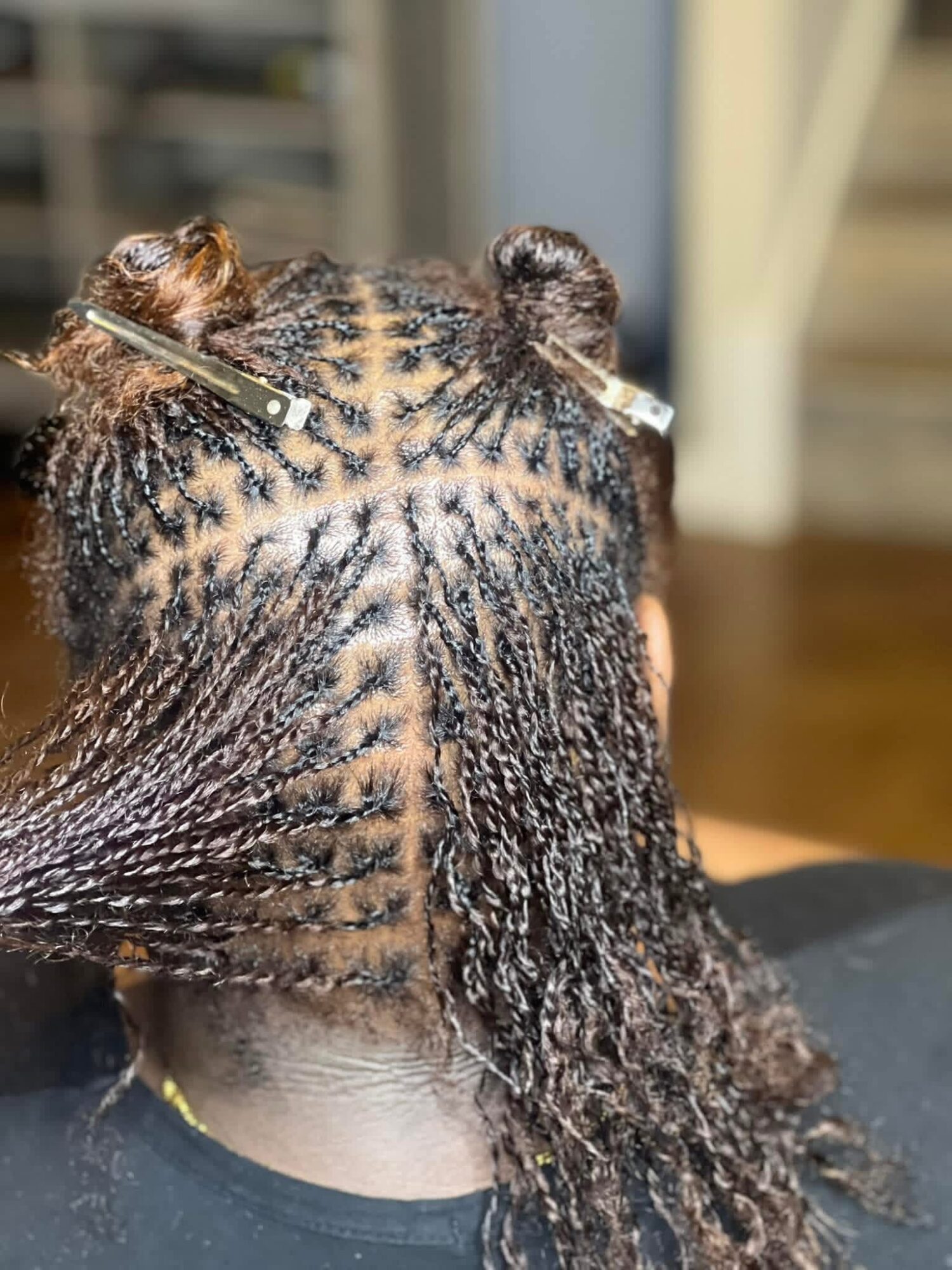 Person's hair sectioned and styled in small twists, with hair clips holding sections, viewed from the back.