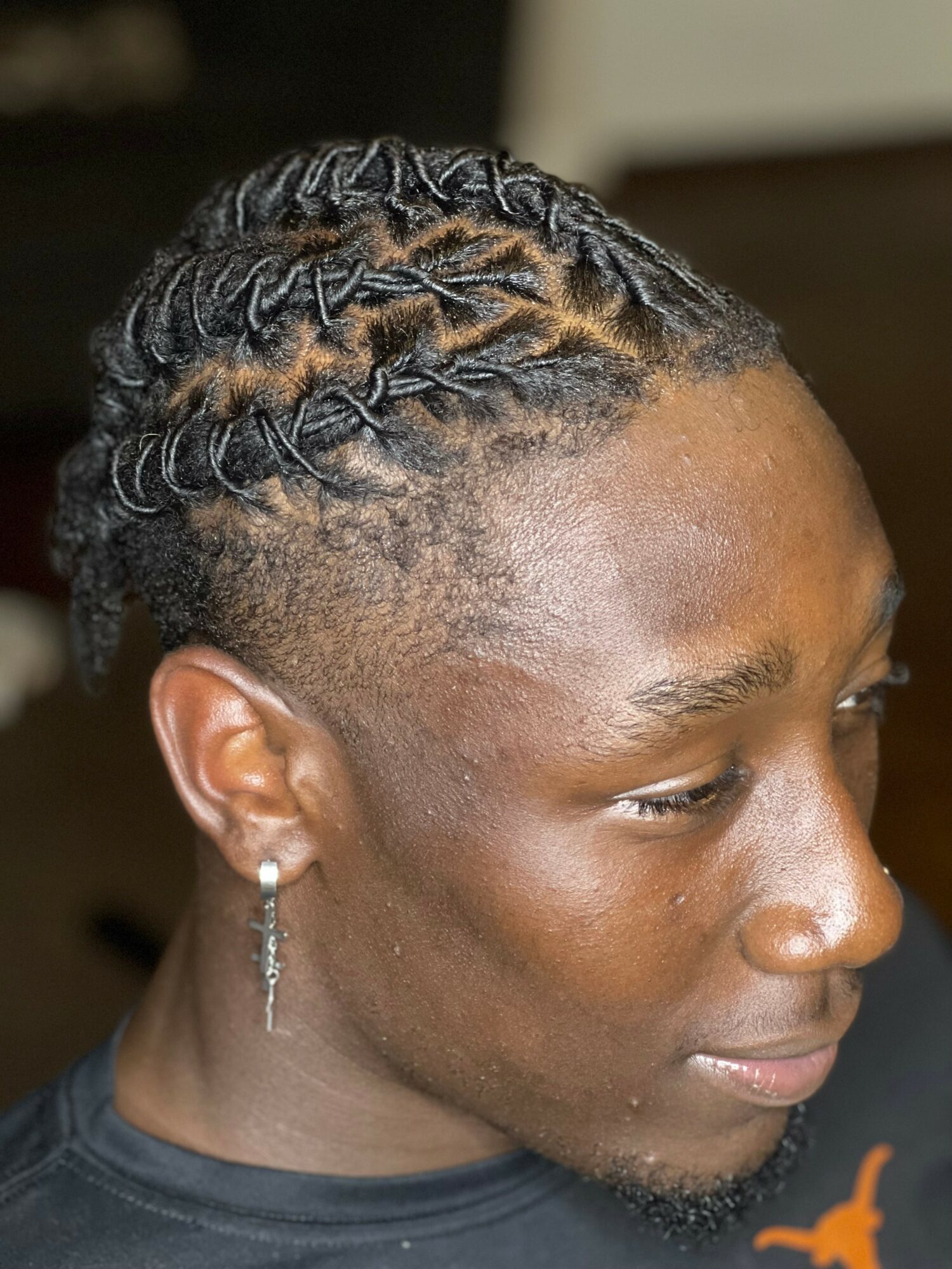 Close-up of a person with braided hairstyle, wearing a hoop earring, looking to the side.