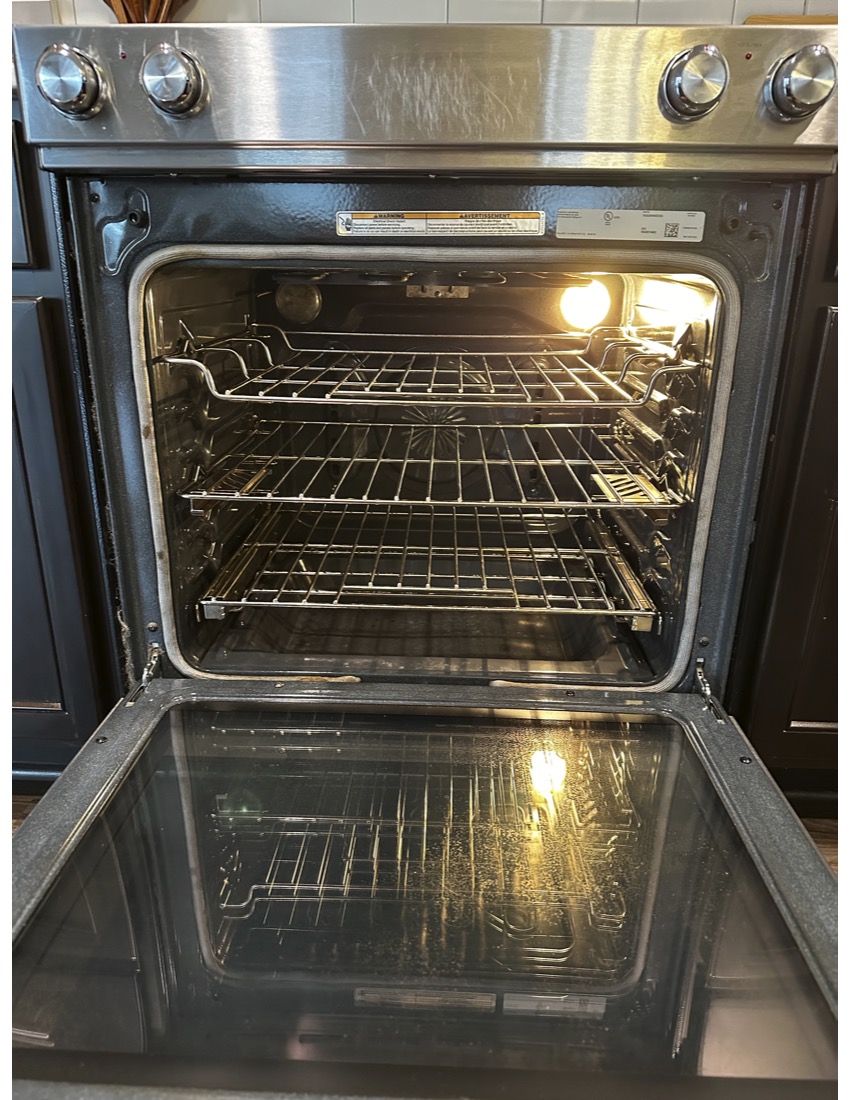 Open oven with empty racks inside, light on, and reflective glass door showing interior reflection.