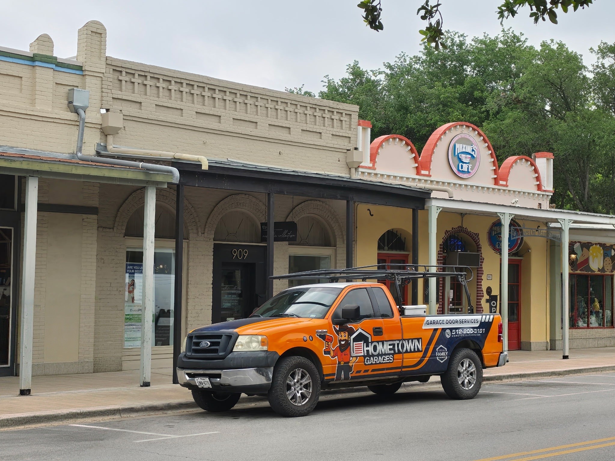 Orange and black Hometown Caretaker vehicle parked in front of a historic building with decorative architecture.