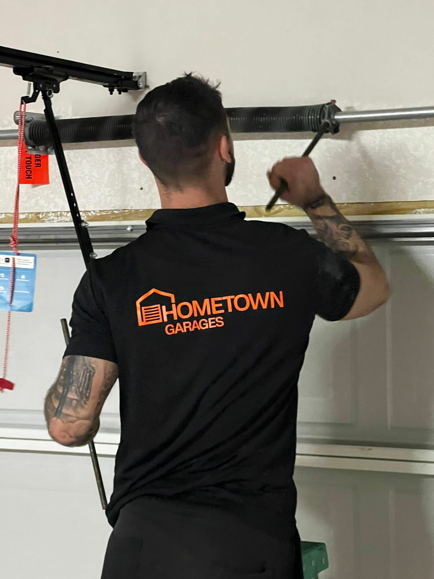 Person working on a plumbing fixture, wearing a black T-shirt with orange text, in a bathroom or similar setting.