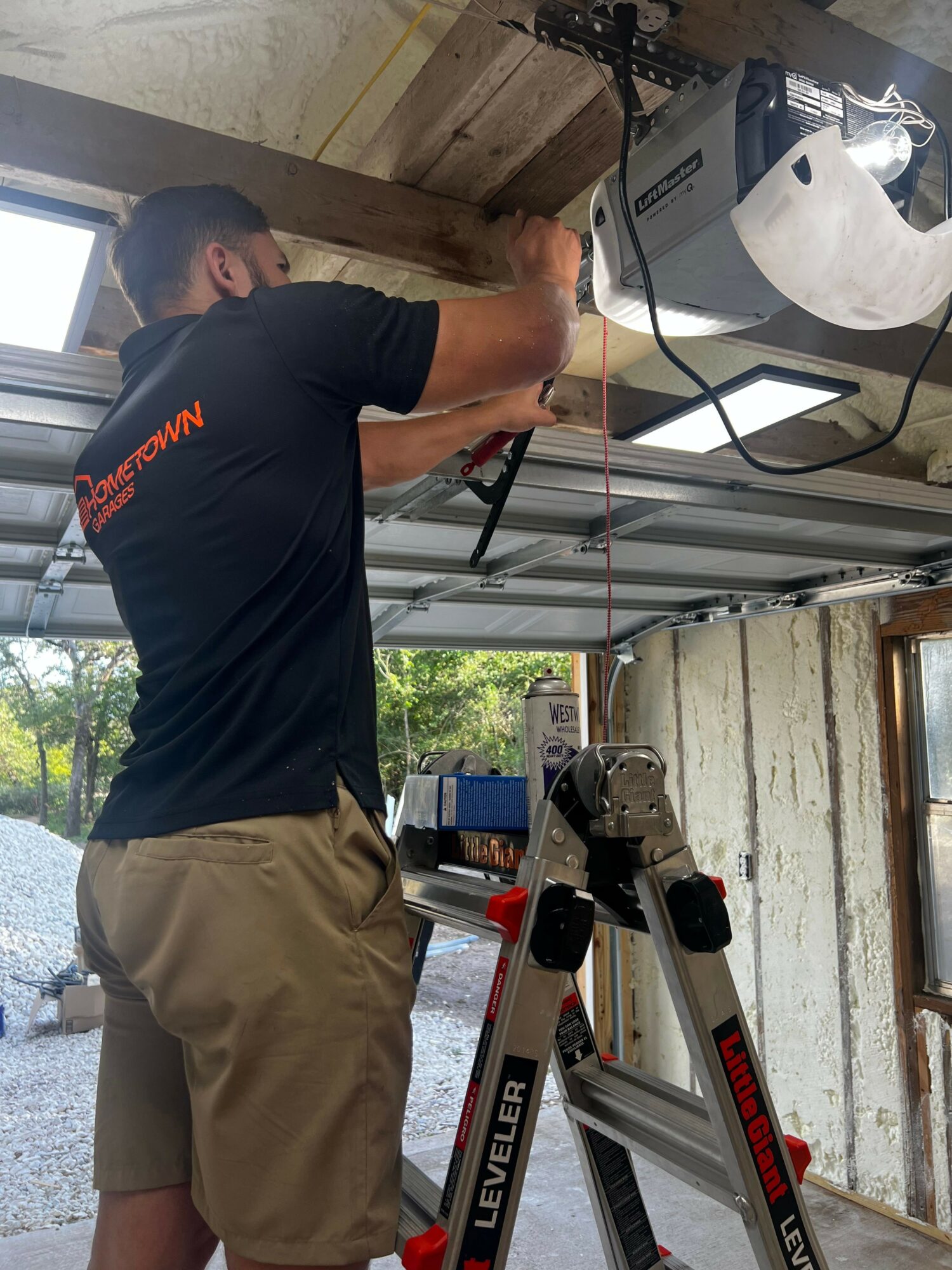 Person working with tools on a wooden surface in a workshop, with equipment and a ladder nearby.