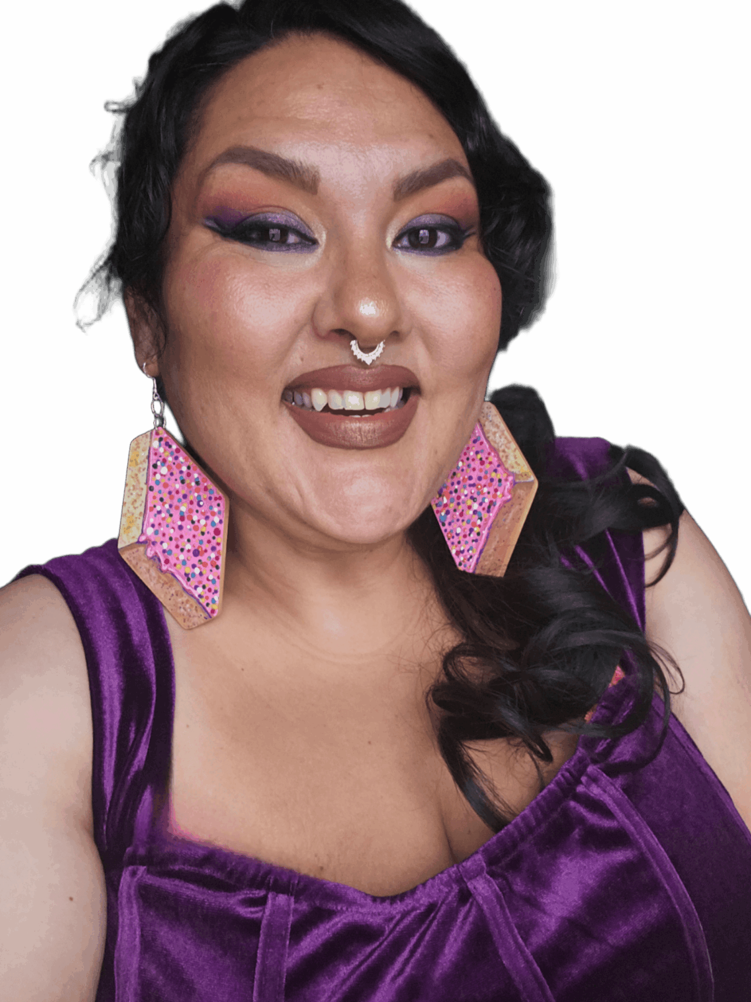 Woman with dark hair, colorful makeup, large pink earrings, purple velvet top, smiling, against a black background.