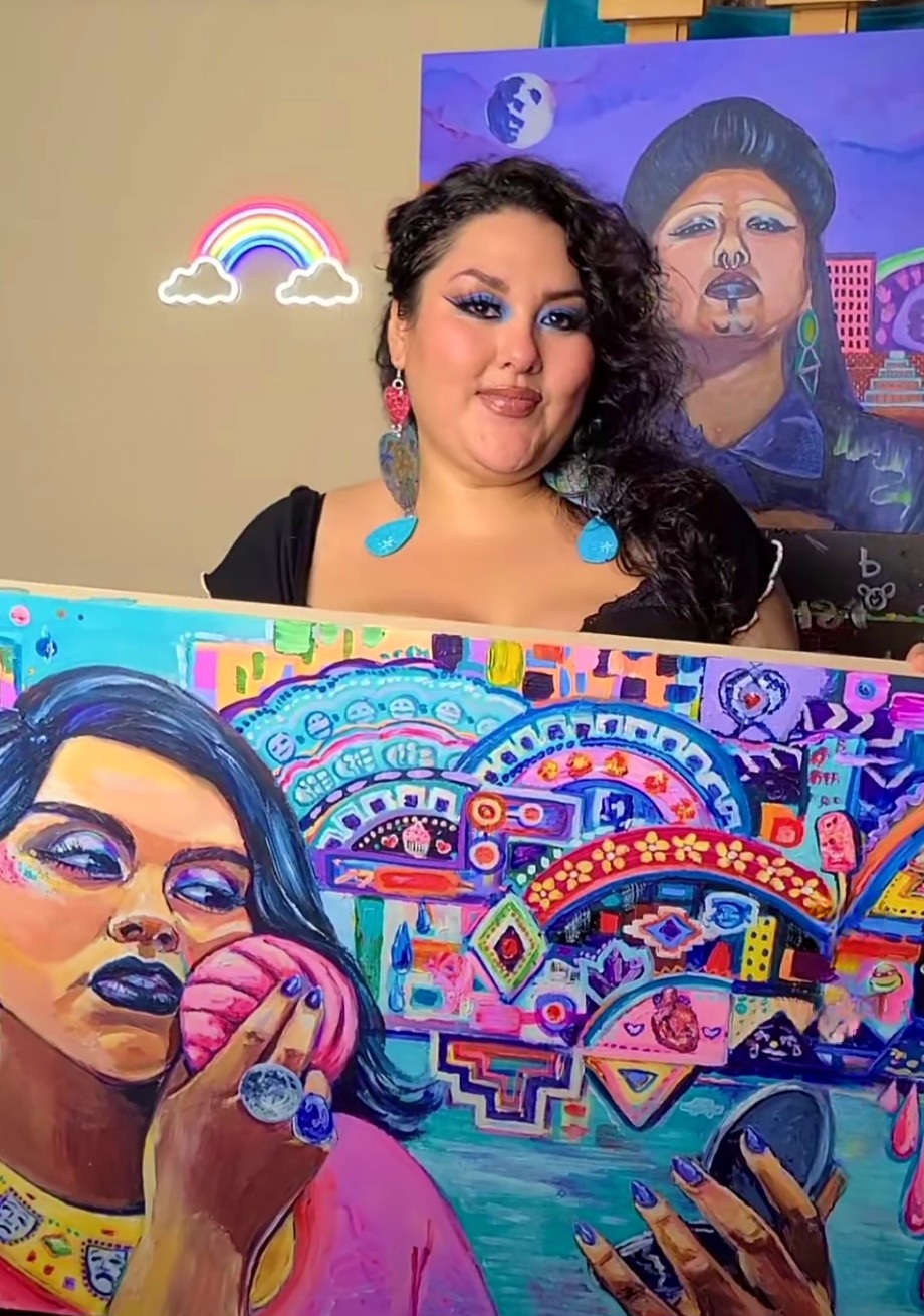 A woman with dark, curly hair and colorful earrings stands in front of vibrant, abstract artwork.