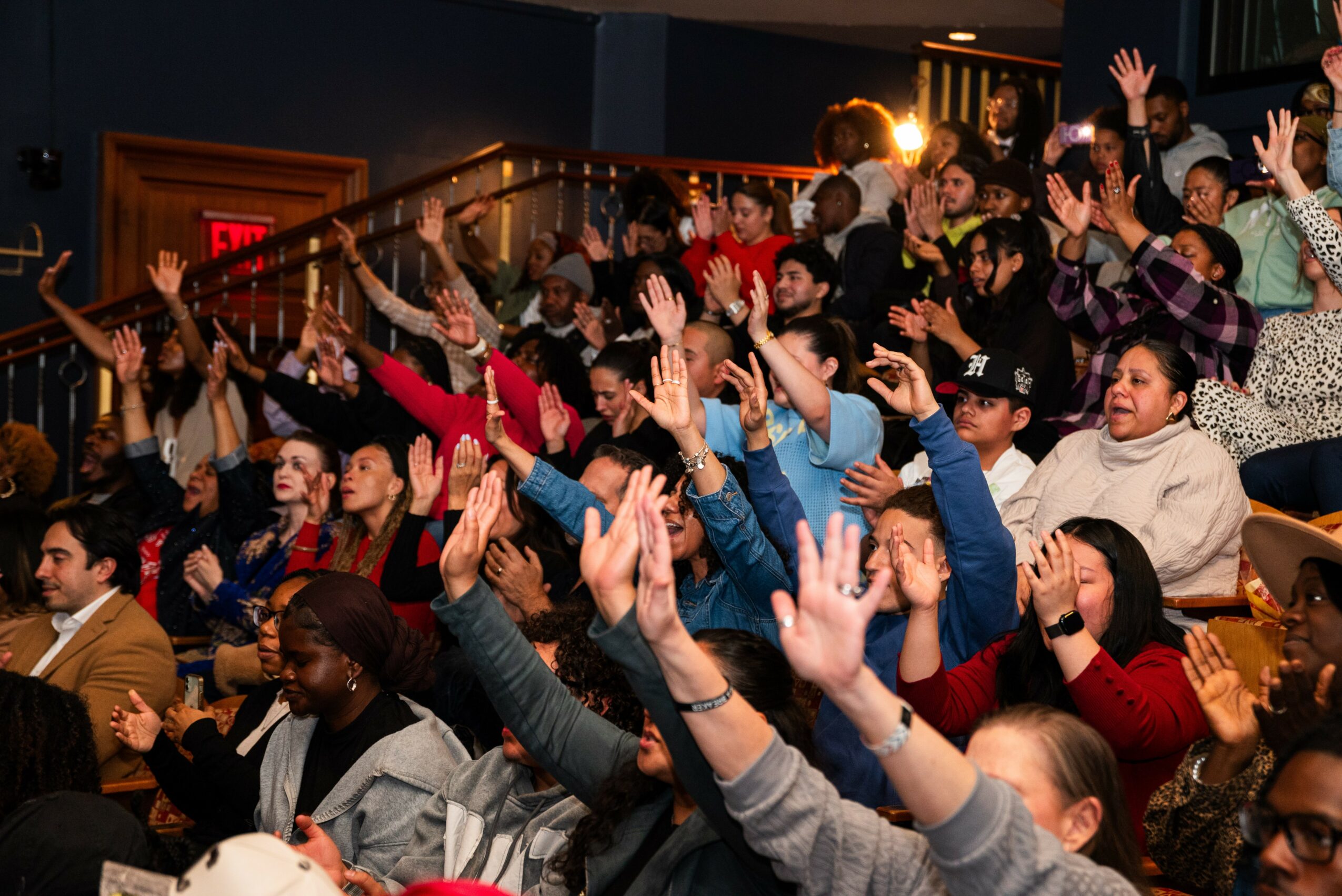 Audience members raising hands and cheering in a theater or auditorium setting.