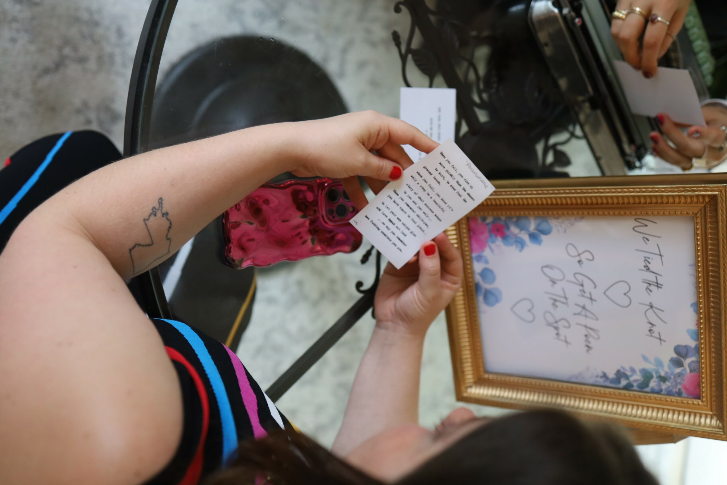 Person holding a framed handwritten note, with another person reading a card, in a room with a table and camera.