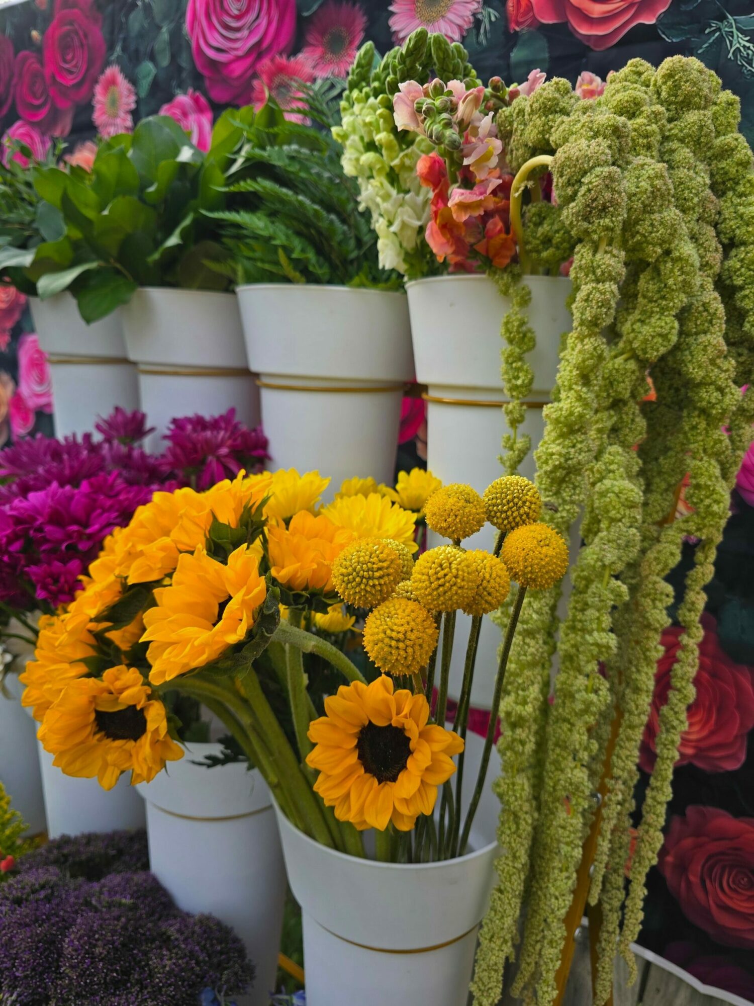 Arrangement of various colorful flowers including yellow sunflowers, pink, purple, and green flowers, with some wrapped in white paper.