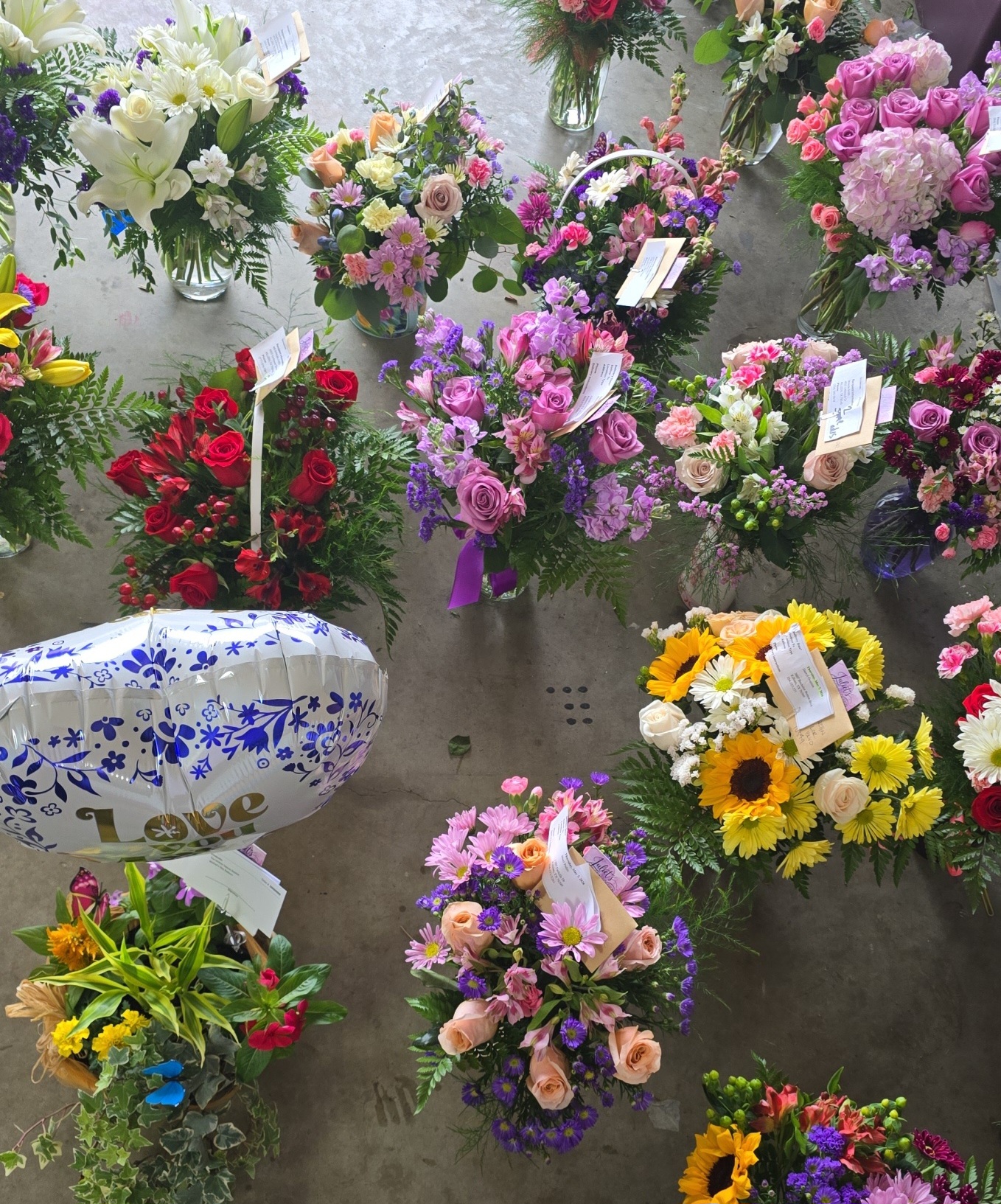 Various colorful flower arrangements and bouquets displayed on a surface, including roses, sunflowers, and other flowers, with some tags visible.