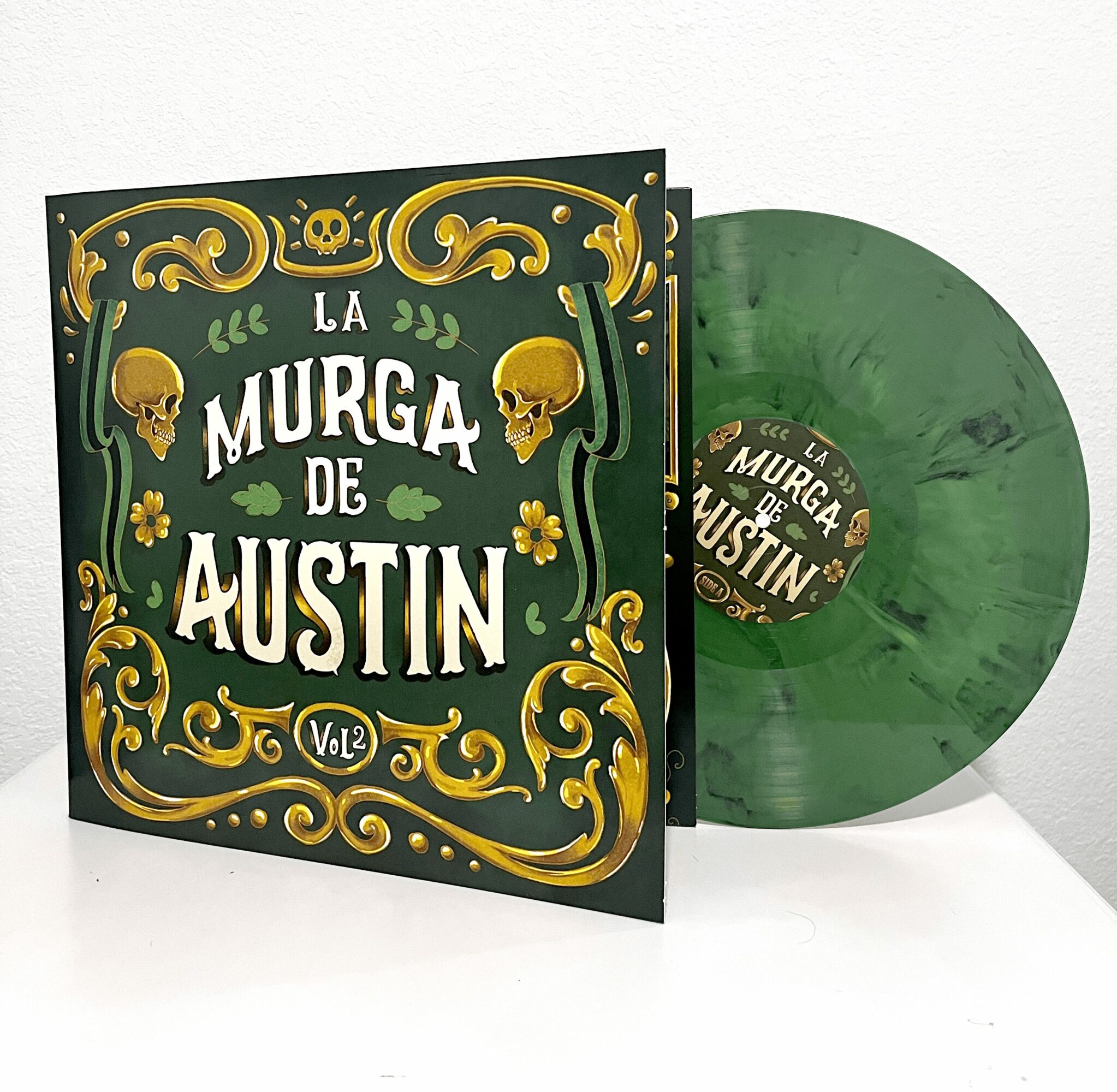 Green vinyl record and album cover with skulls and decorative elements, titled 'La Murga de Austin Vol.2'.