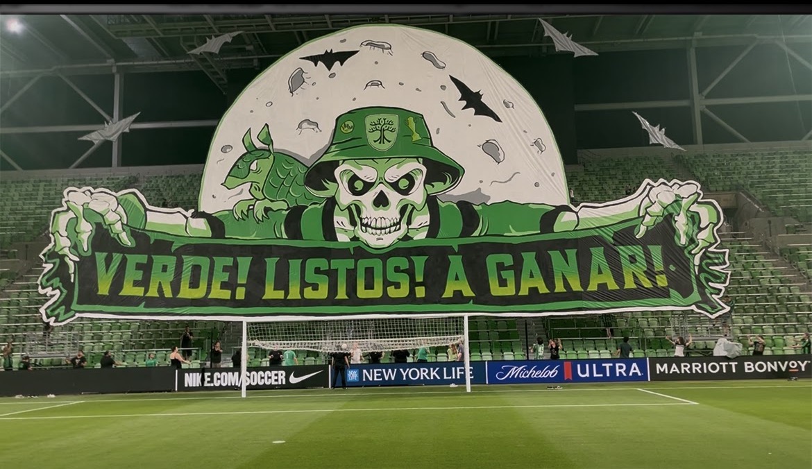 Large banner with a skull wearing a green hat, holding a sign that says 'VERDE! LISTOS! A GANAR!' in a stadium.
