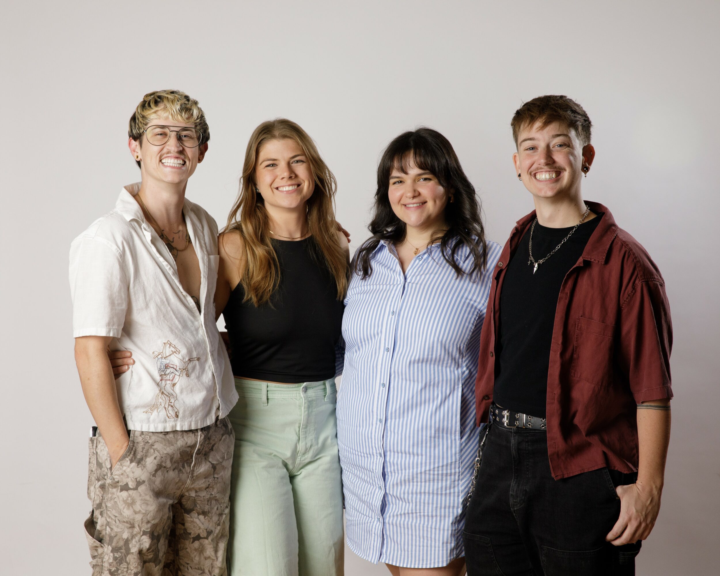 Four people standing together, smiling, against a plain background.