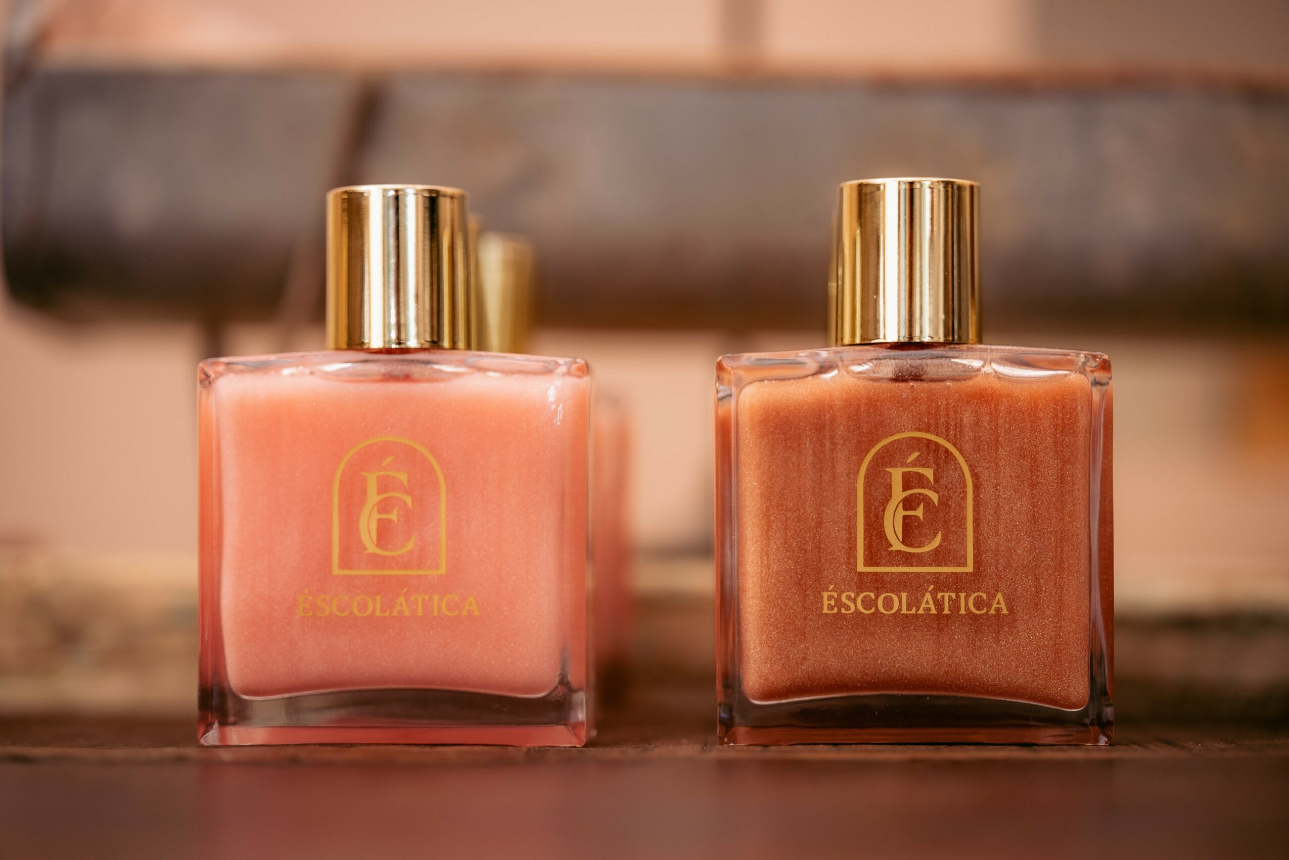 Two square perfume bottles with gold caps, one pink and one brown, on a wooden surface, blurred background.