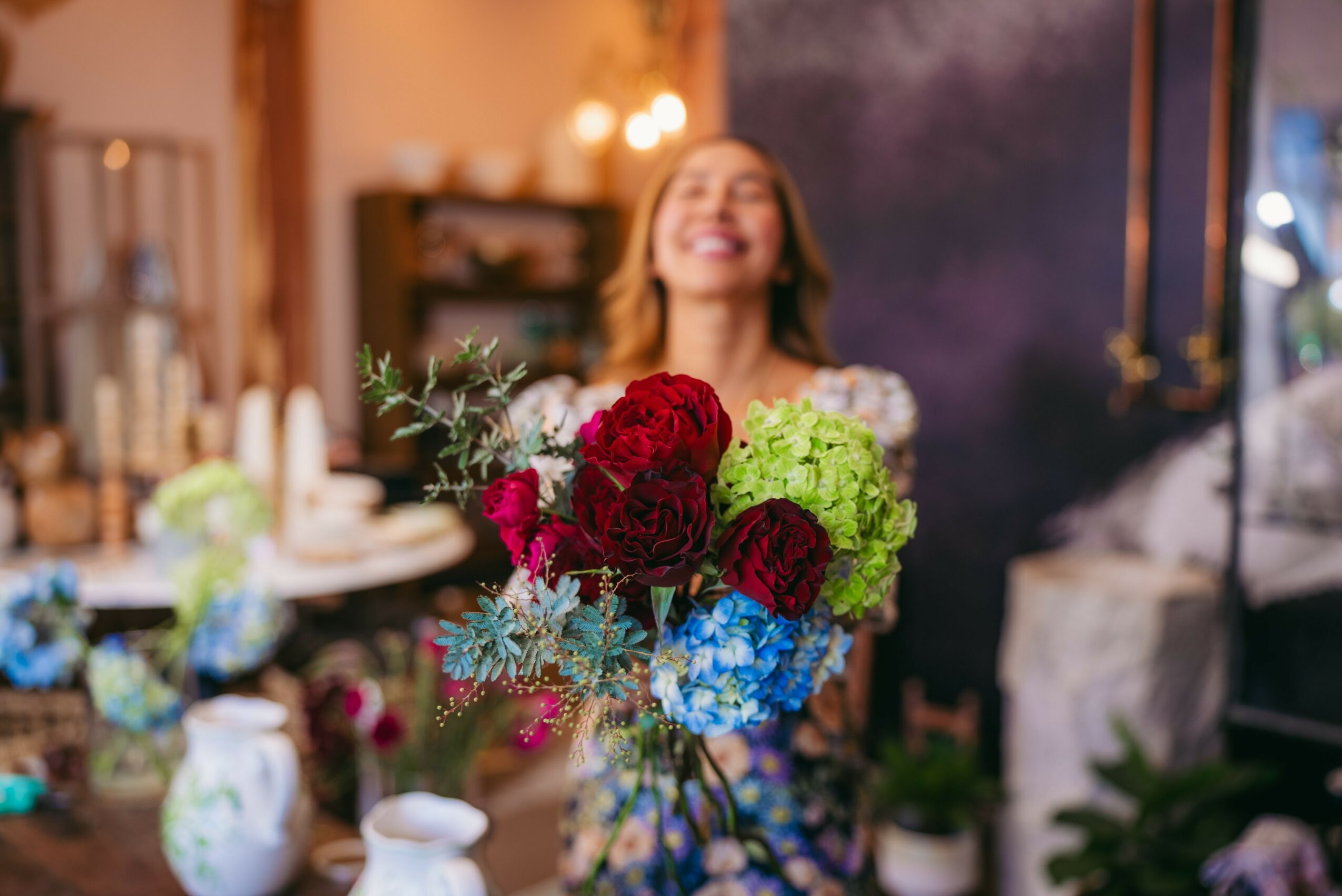Person holding a colorful bouquet of flowers, smiling in a cozy indoor setting.