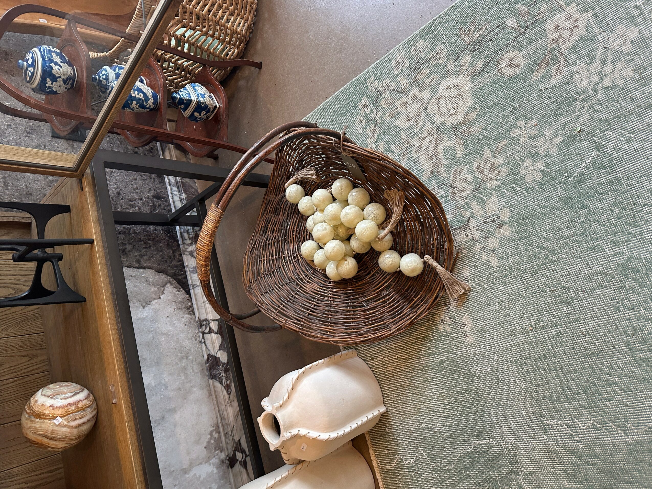 Basket filled with white balls on a green rug, with a ceramic object nearby and furniture in the background.