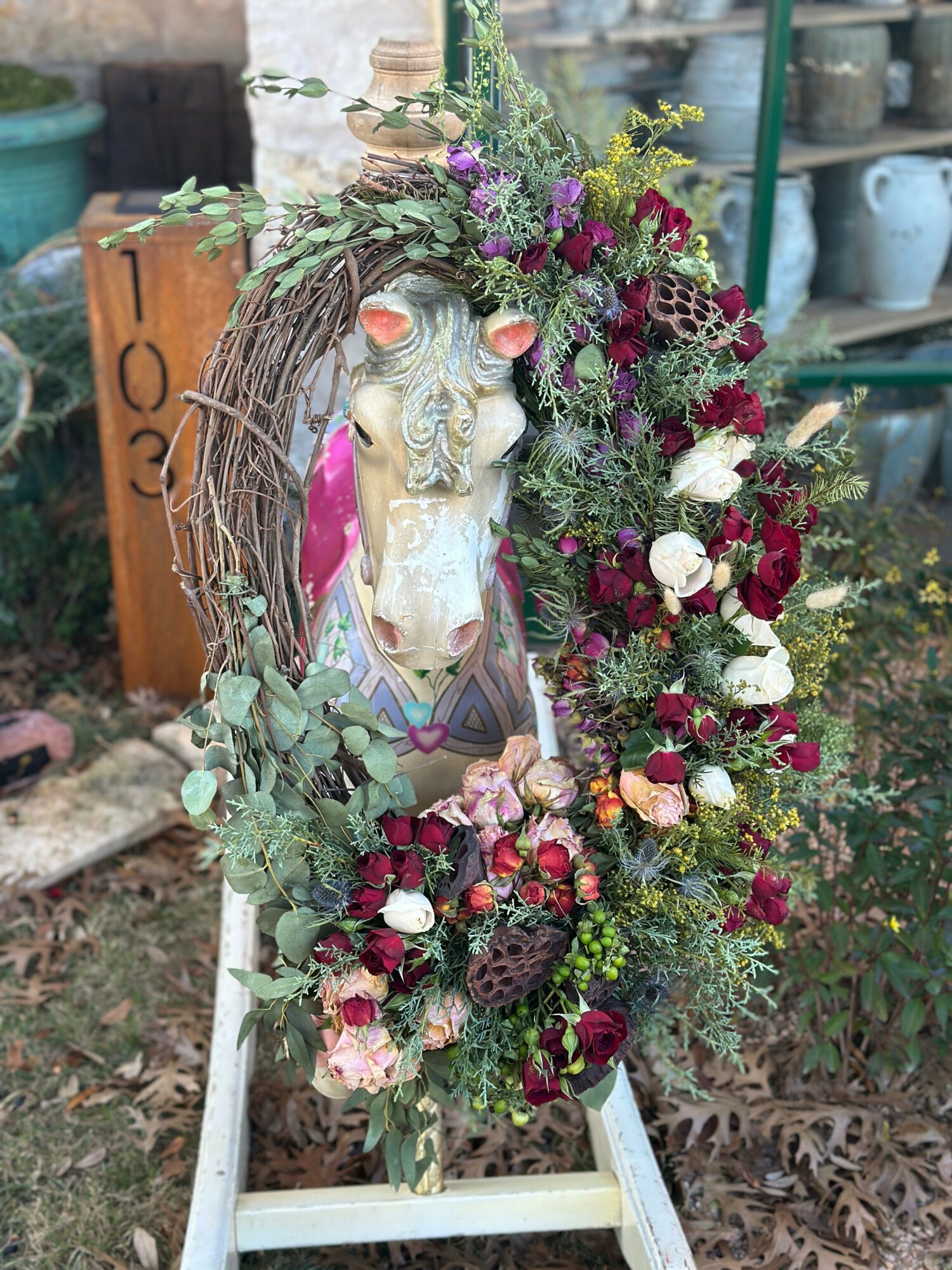 Decorative floral arrangement with a horse head sculpture surrounded by purple, white, and pink flowers and greenery.