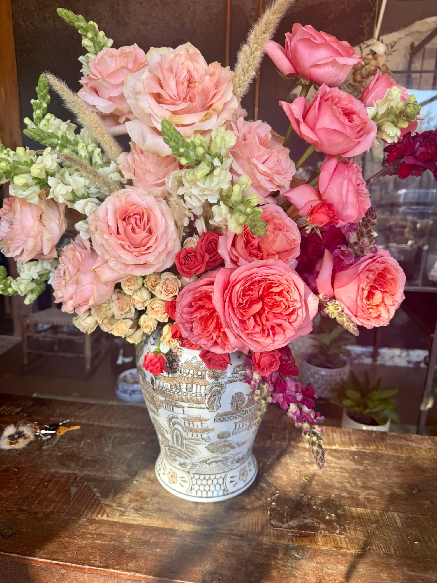 Pink and white flowers in a decorative vase on a wooden surface.
