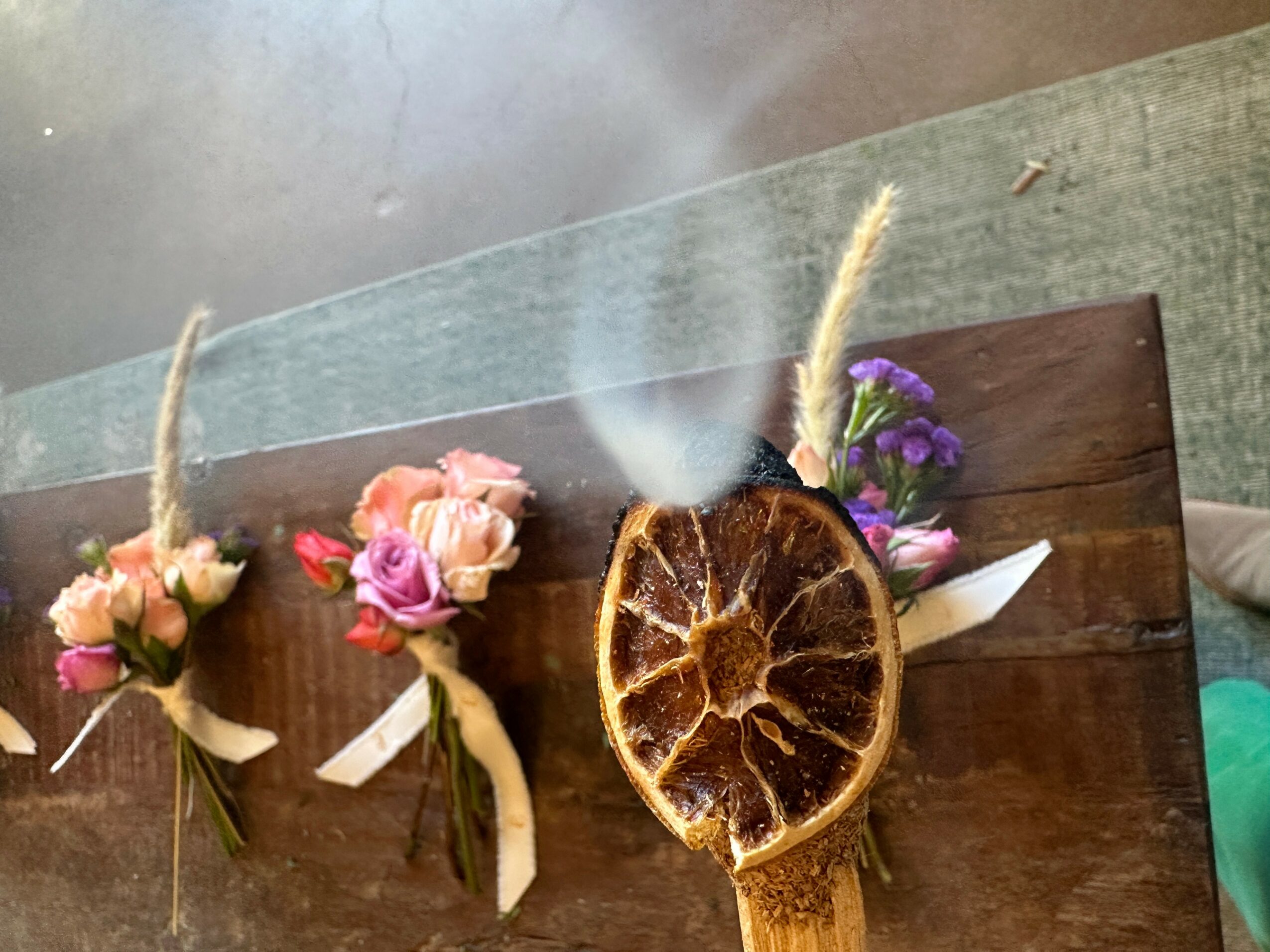 Decorative arrangement with dried citrus slice, flowers, and ribbons on a wooden surface.