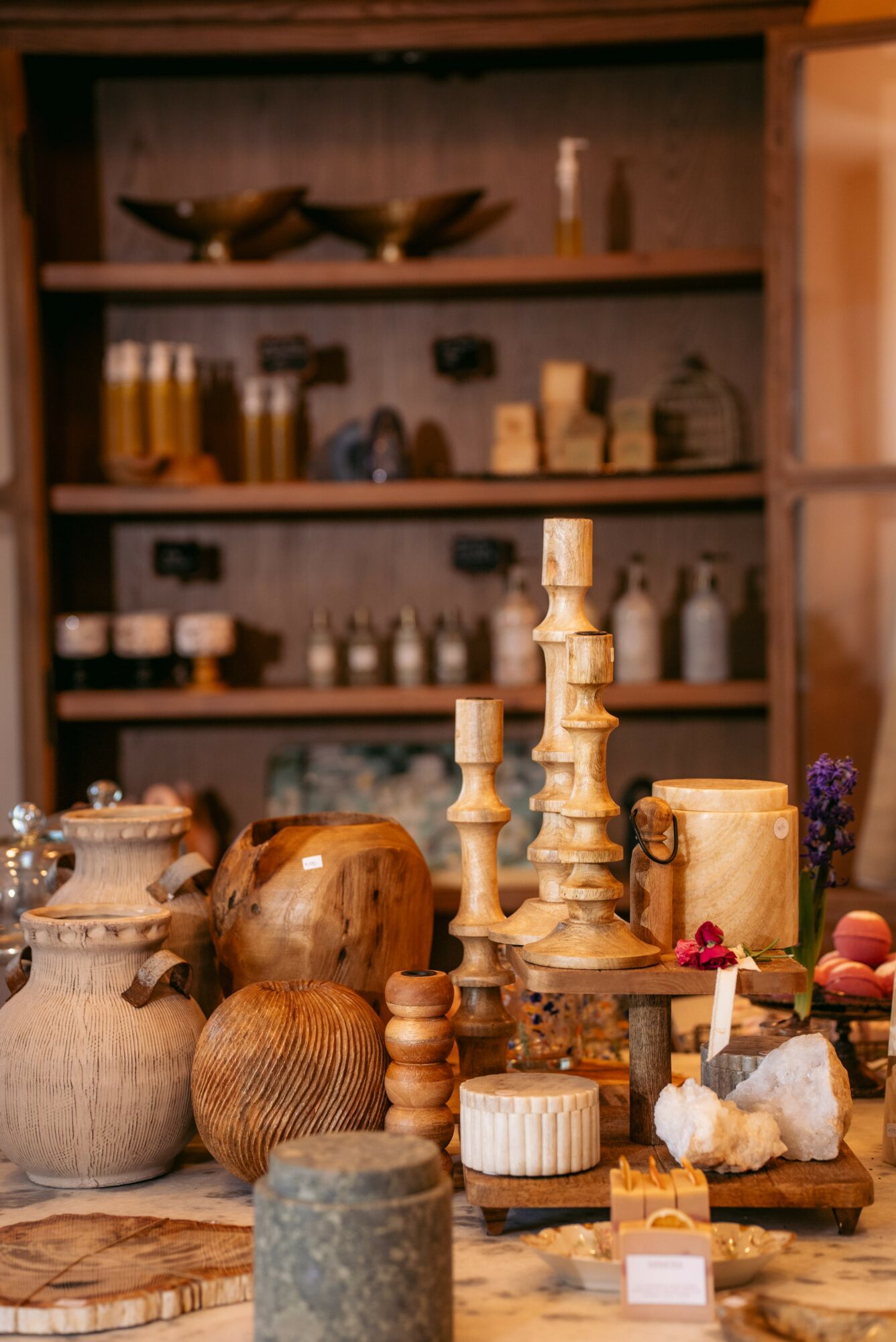 Display of pottery, candles, and decorative items on a wooden table with shelves in the background.