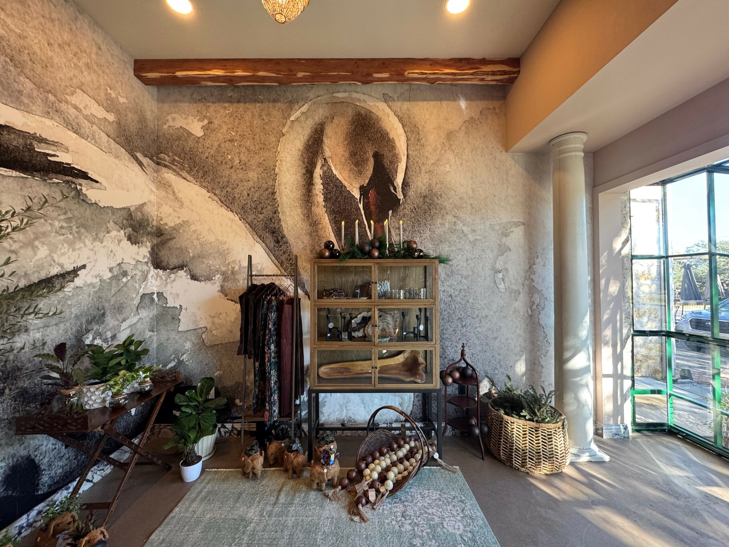 Interior of a room with a textured wall, a wooden shelf with bottles, plants, and decorative items, and a sliding glass door.