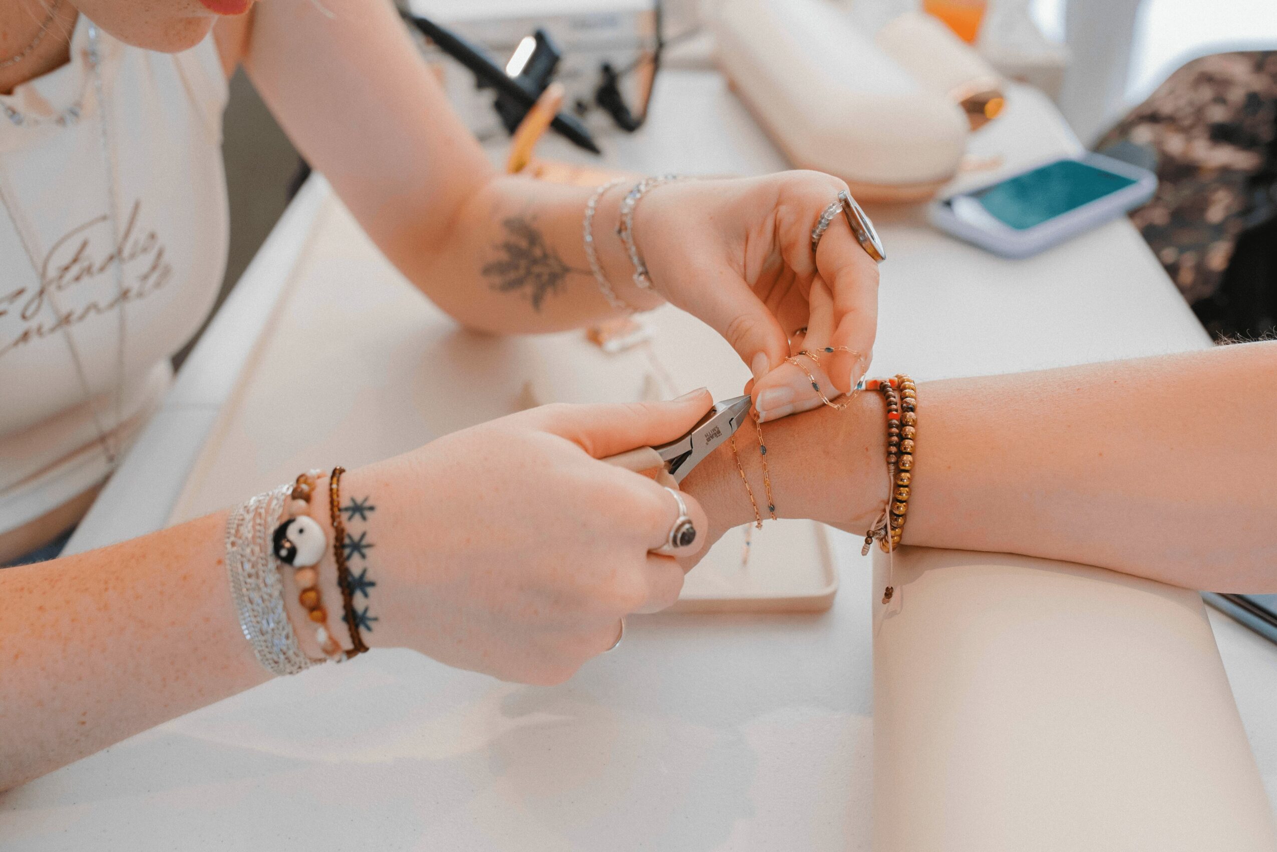 Person applying nail polish to another person's fingernail, with various bracelets on both wrists, on a white table.