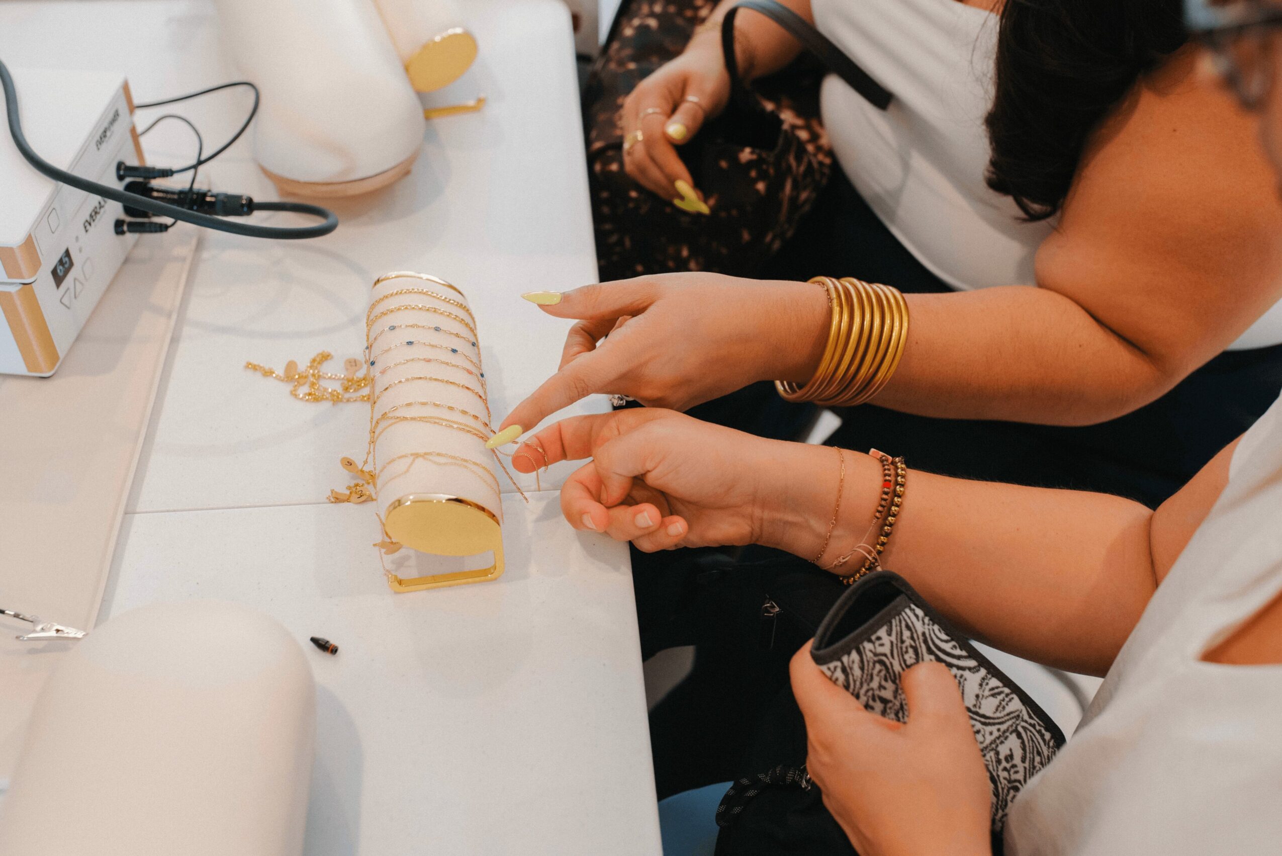 People sitting at a table with a rolled cake, hands with jewelry, and a phone, in a well-lit room.