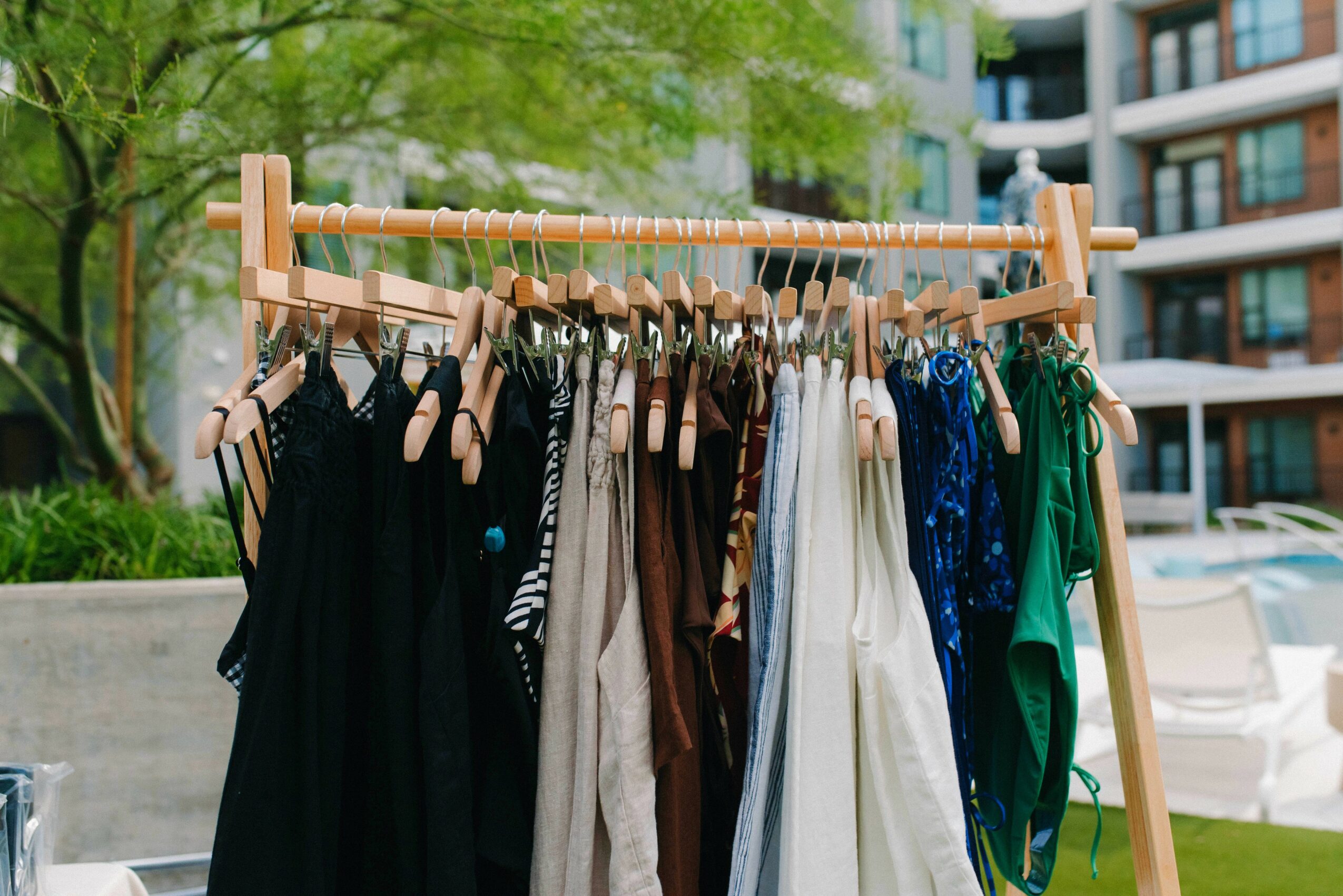 Clothing rack with various dresses and garments outdoors, with trees and buildings in the background.