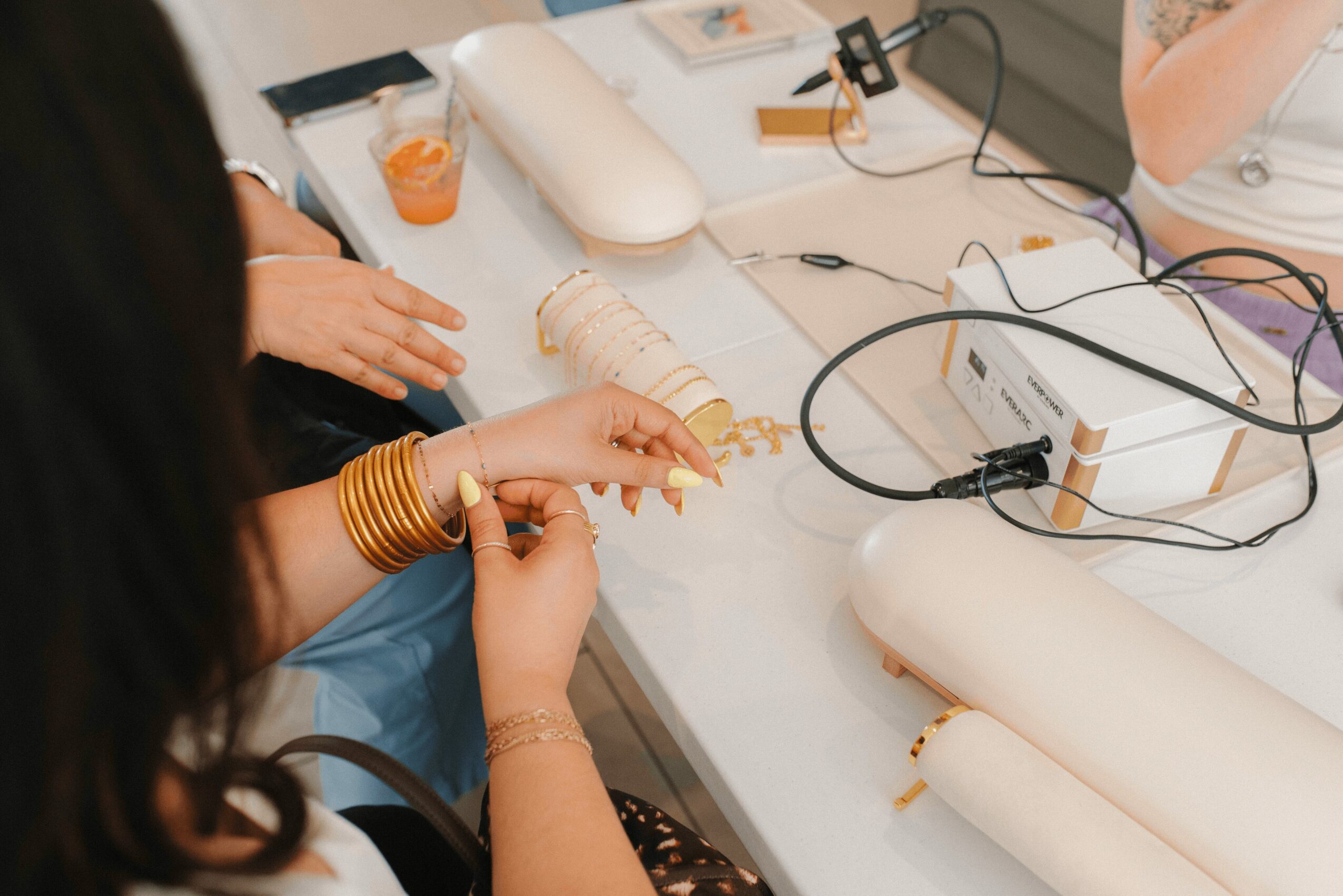 Person wearing gold bangles working with gold jewelry on a white table with various tools and materials.