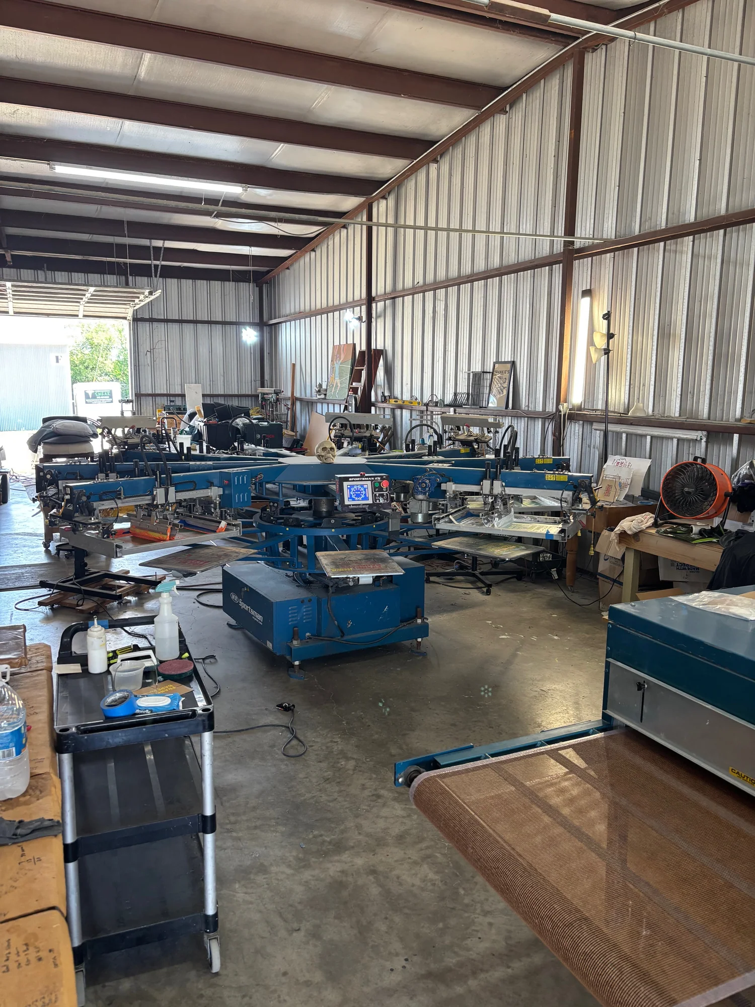 Industrial workshop with machinery and tools, metal walls, and a concrete floor, organized workspace with equipment and supplies.