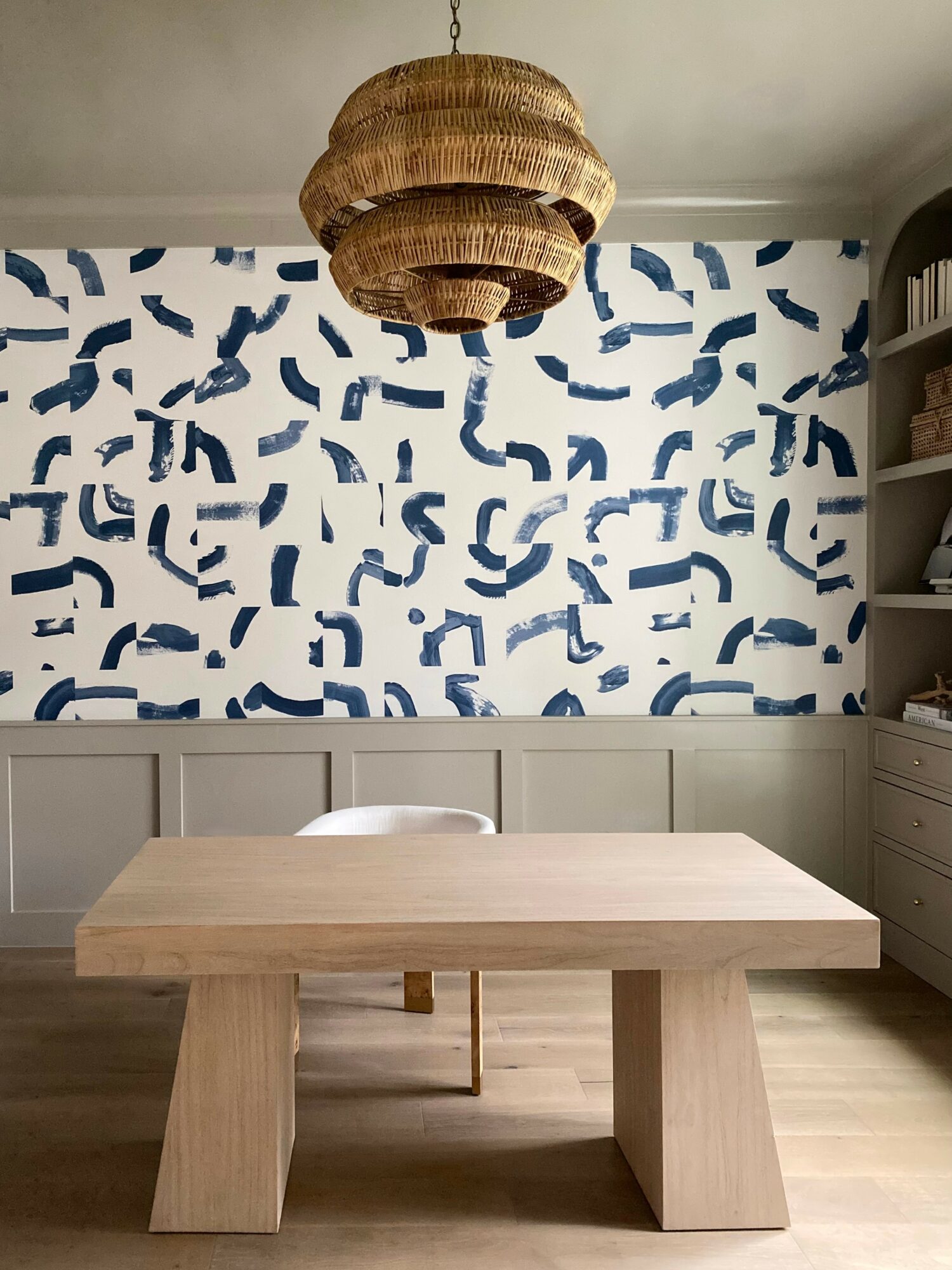 Room with a wooden table, patterned blue and white wallpaper, and a woven chandelier hanging from the ceiling.