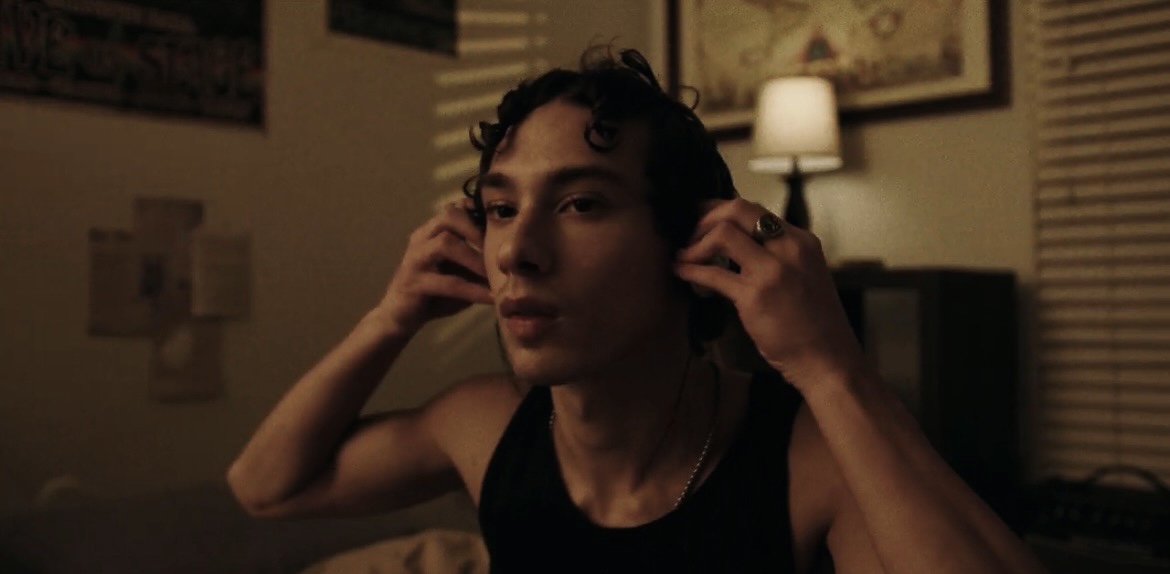 Person adjusting headphones in a dimly lit room with a lamp and window blinds behind them.