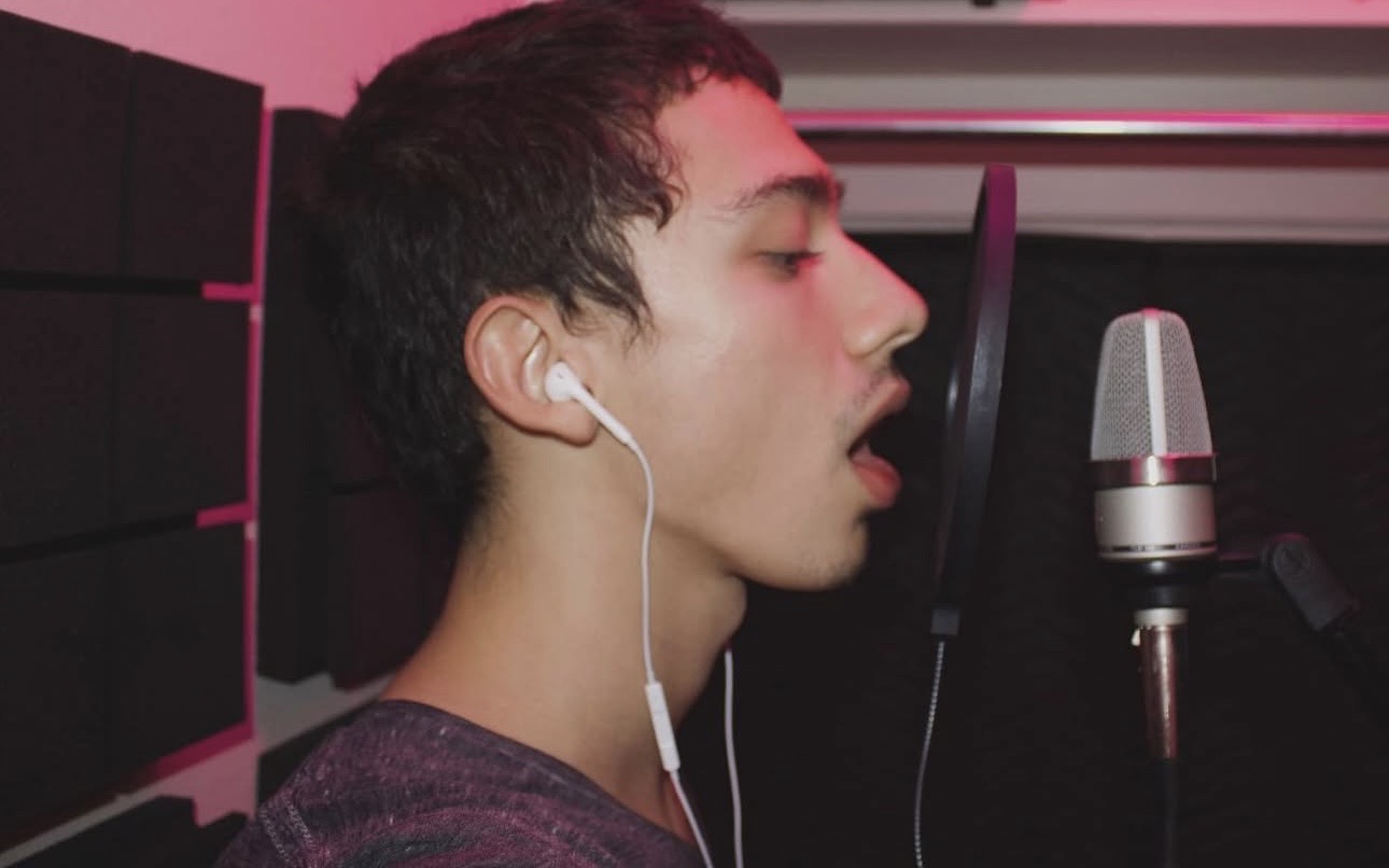 Young man with earphones singing into a microphone in a recording studio.