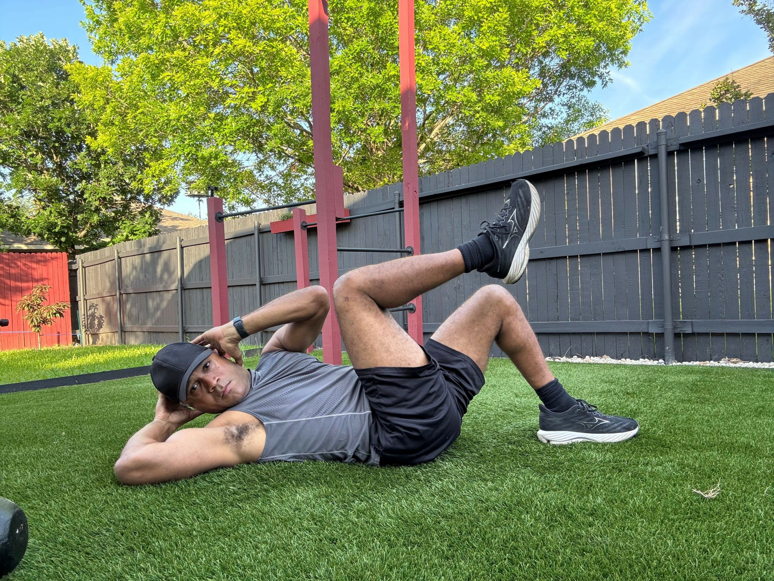 Person in athletic clothing leaning on a red railing outdoors, with green grass and trees in the background.