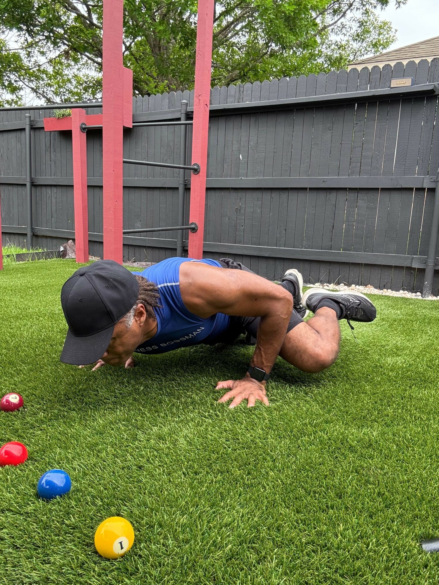 Person sitting on grass near a fence, surrounded by colorful balls, wearing a black cap and blue shorts.