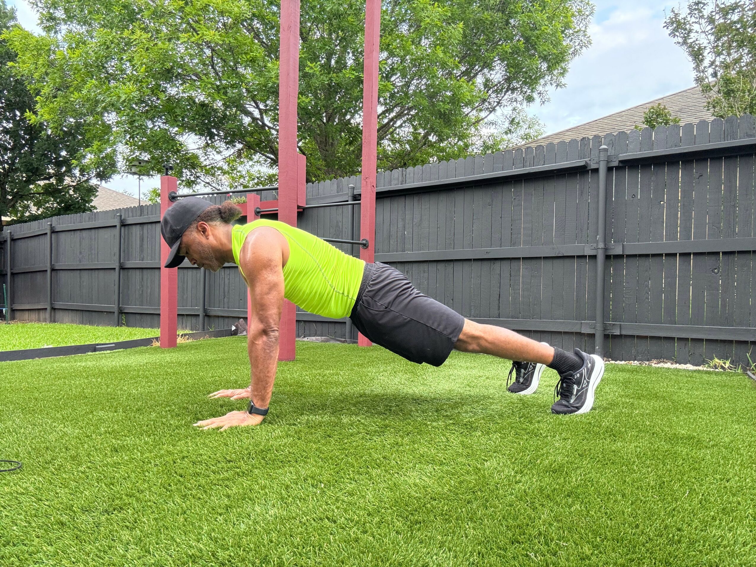 Person performing a push-up outdoors on grass, wearing a bright green tank top and black shorts.