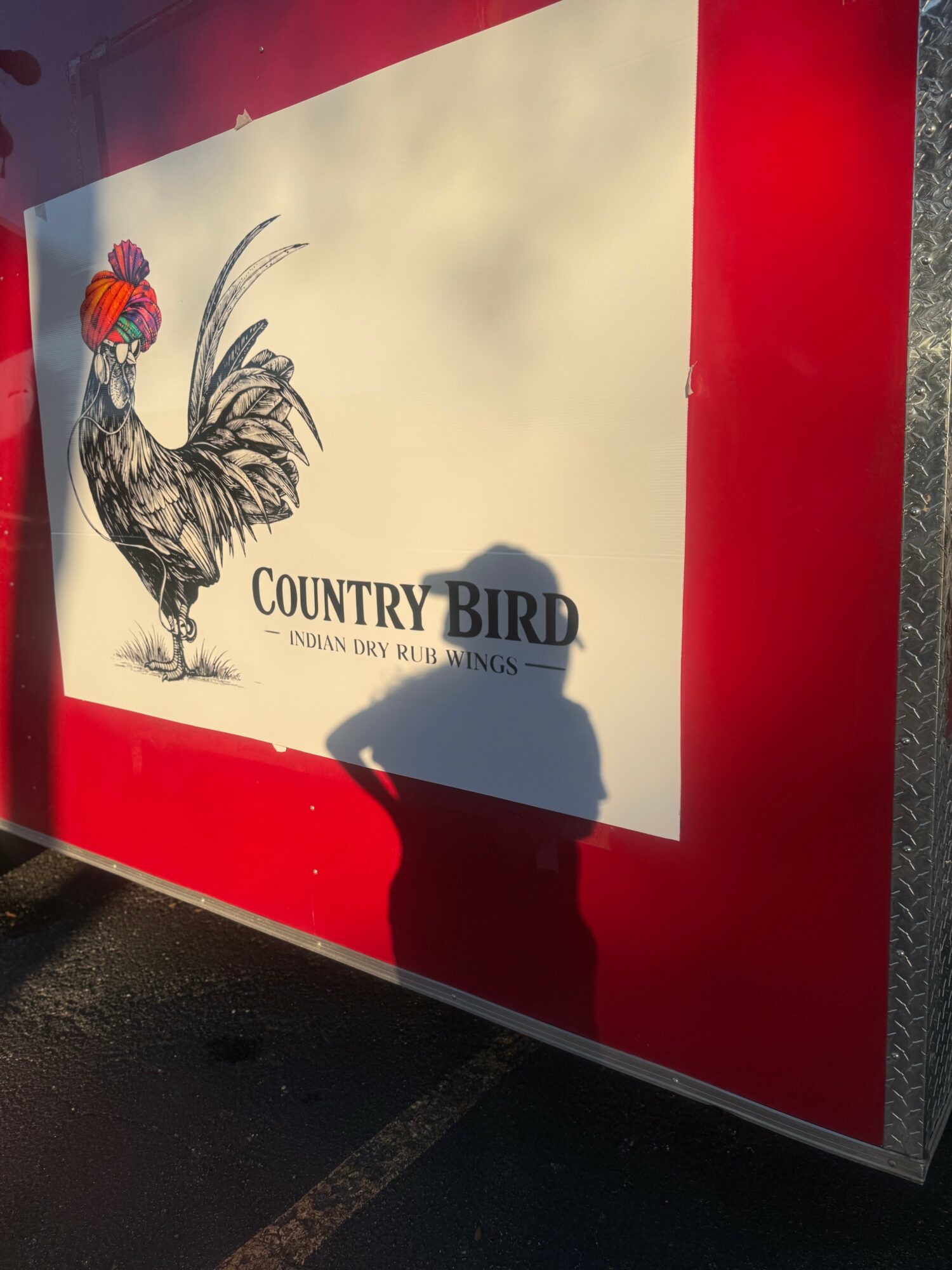 Sign with a colorful bird illustration, text reading 'Country Bird' and additional smaller text, shadow of a person in front.