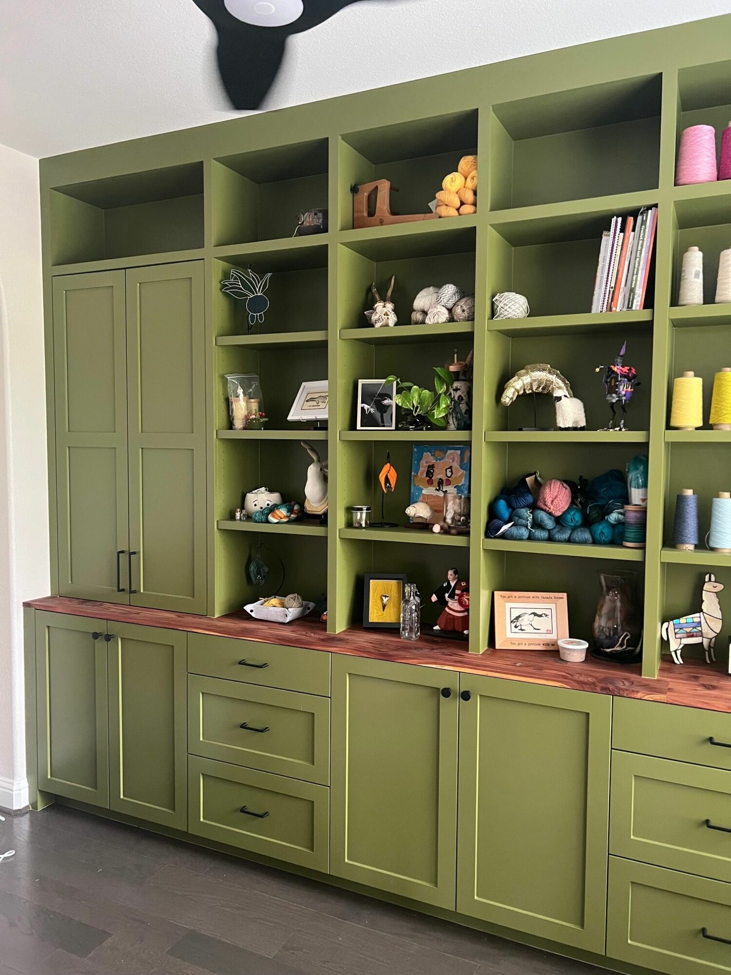 Green bookshelf with multiple compartments filled with books, decorations, and small objects, against a white wall.