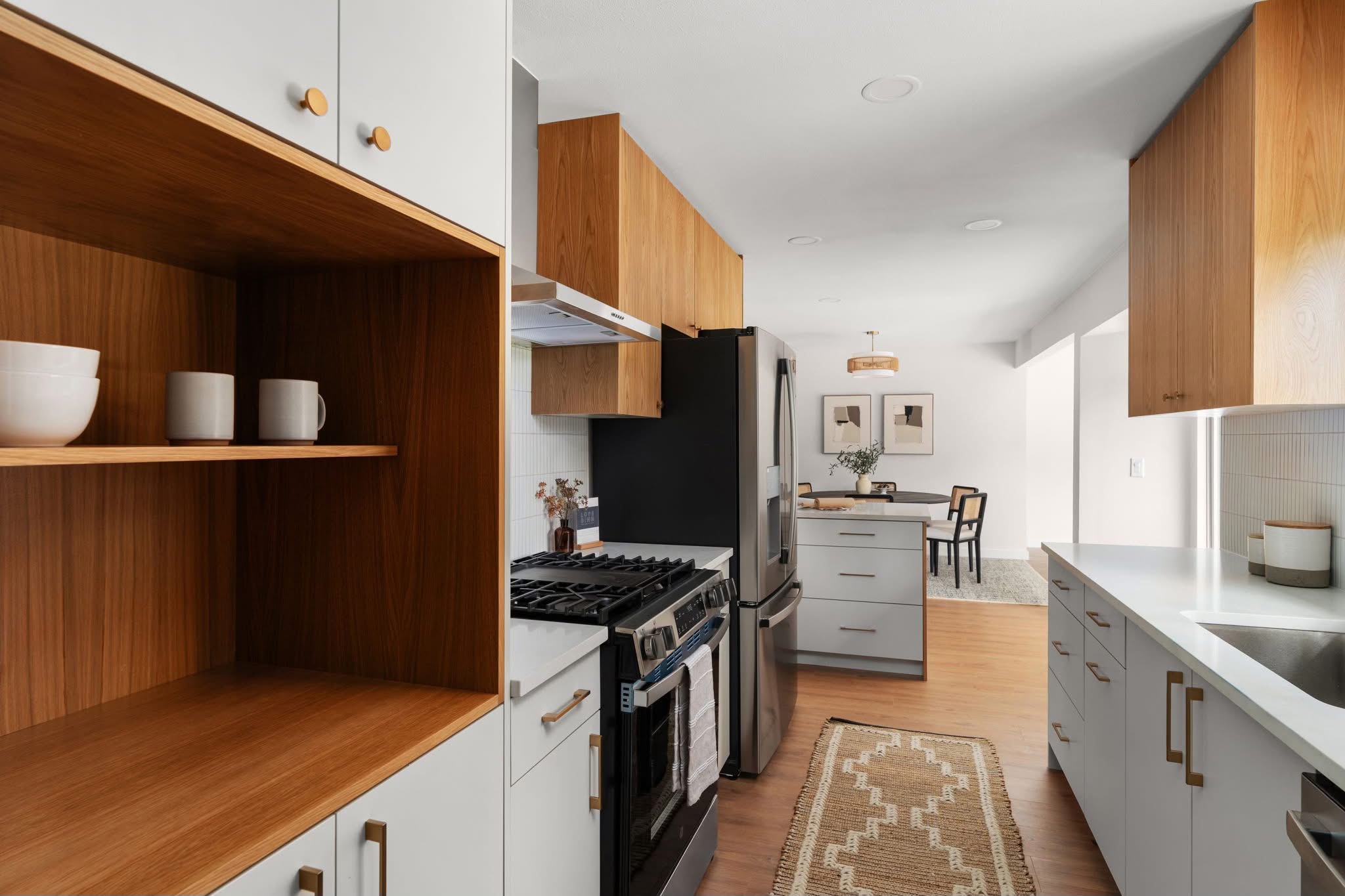 Kitchen with white cabinets, wooden shelves, stainless steel appliances, and a dining area in the background.