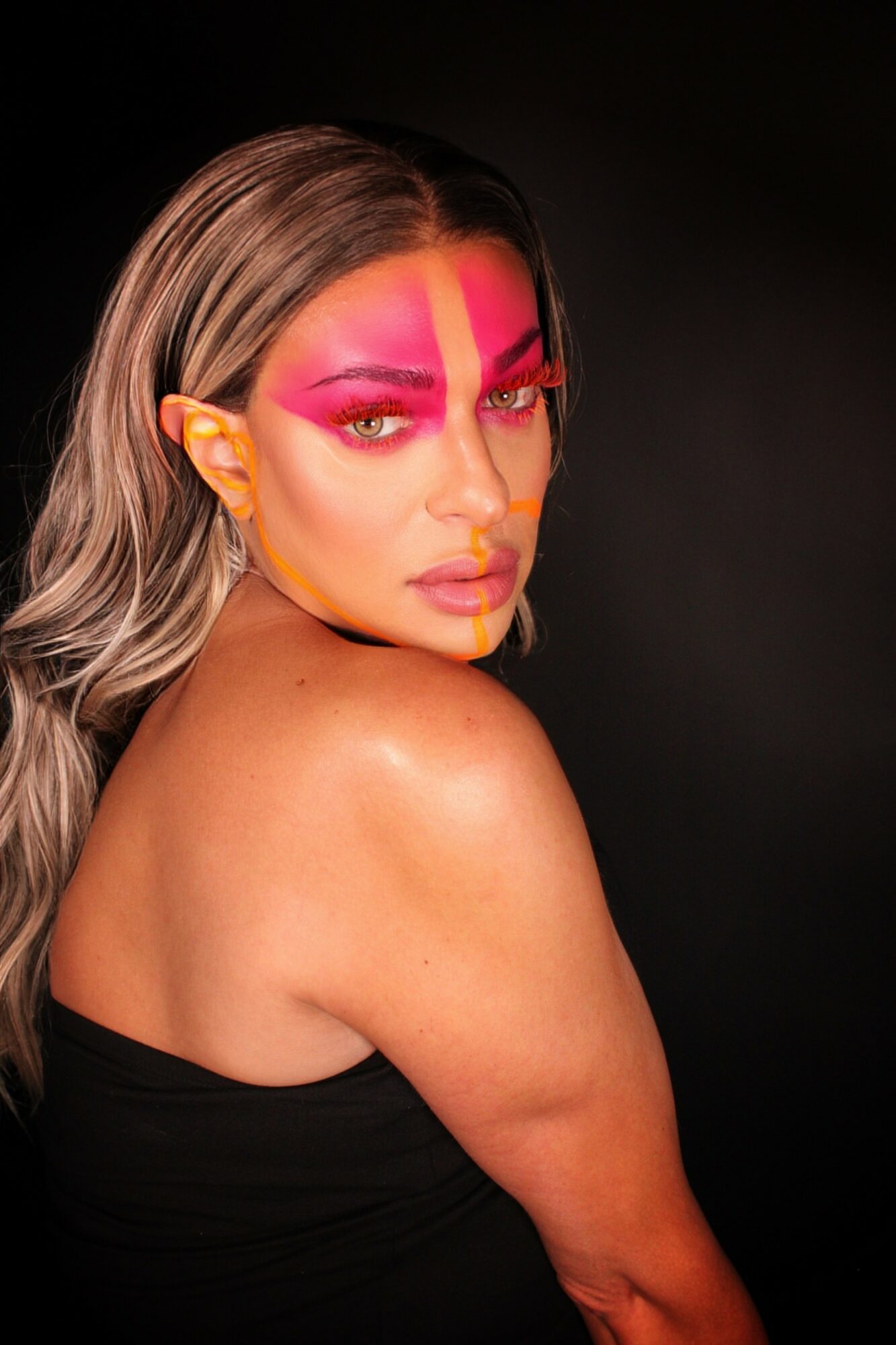 Woman with pink makeup and long hair, looking over shoulder against black background.