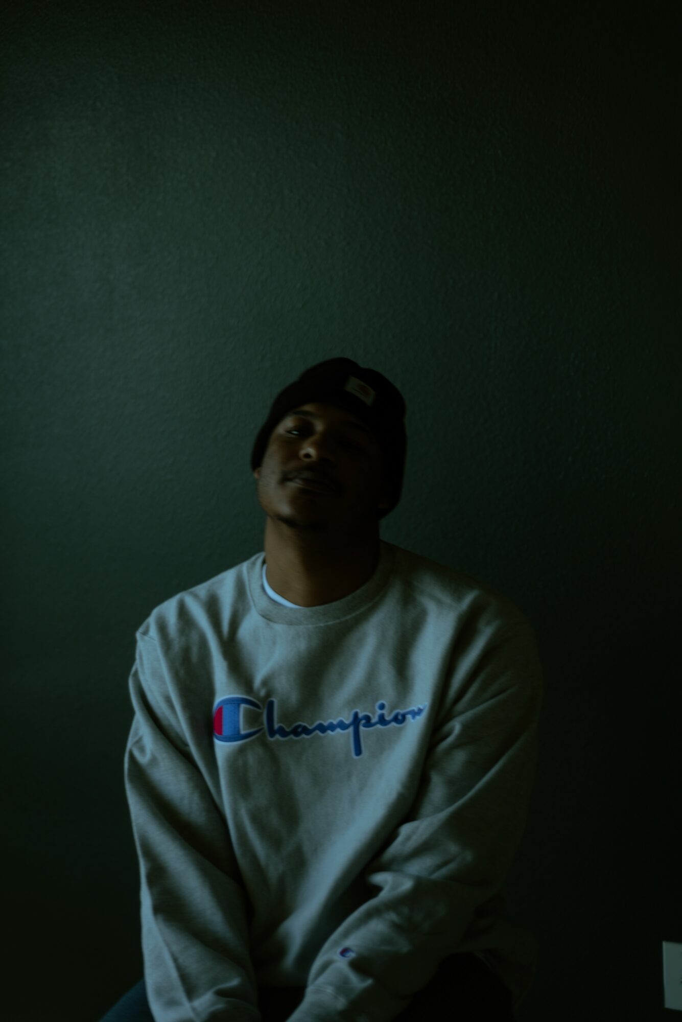 Person wearing a white sweatshirt and a cap, sitting against a dark background.