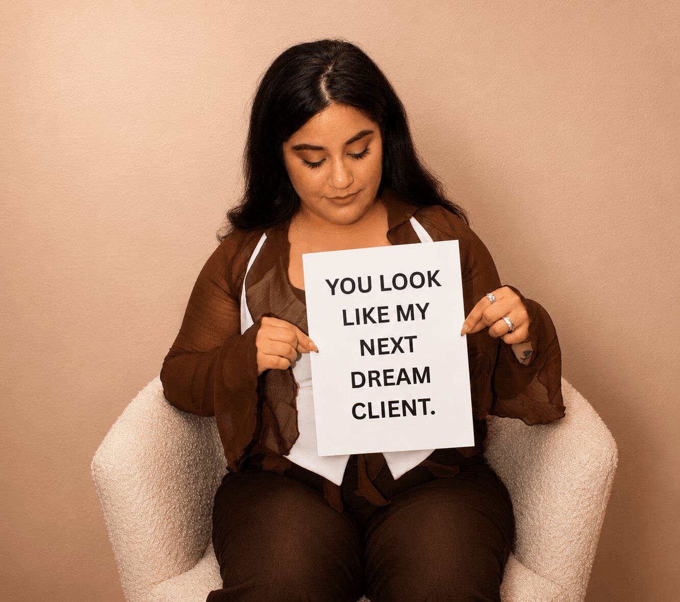 Woman sitting in chair holding a sign that says, 'You look like my next dream client.'