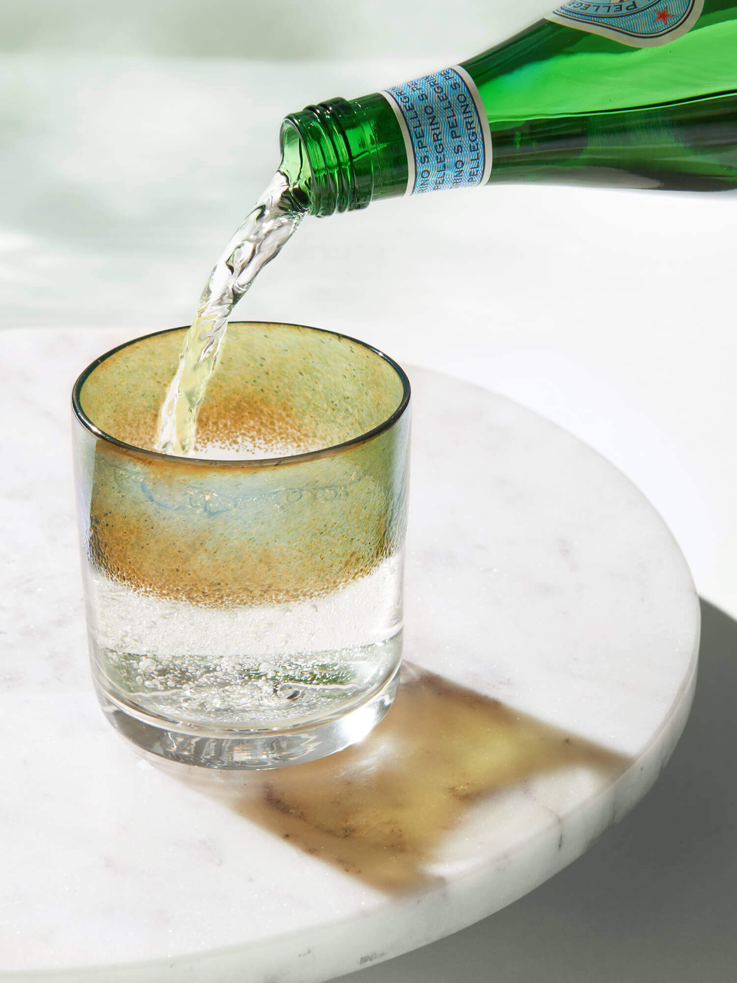 Green bottle pouring clear liquid into a glass on a white surface.