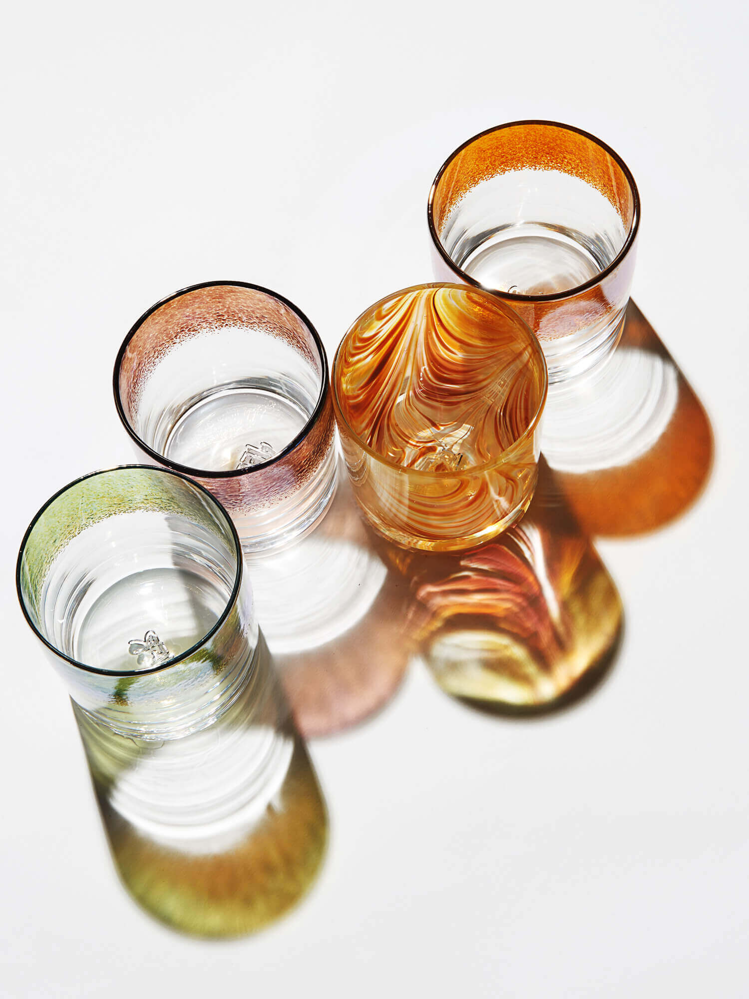 Three colorful glasses with reflections and shadows on a white surface, viewed from above.
