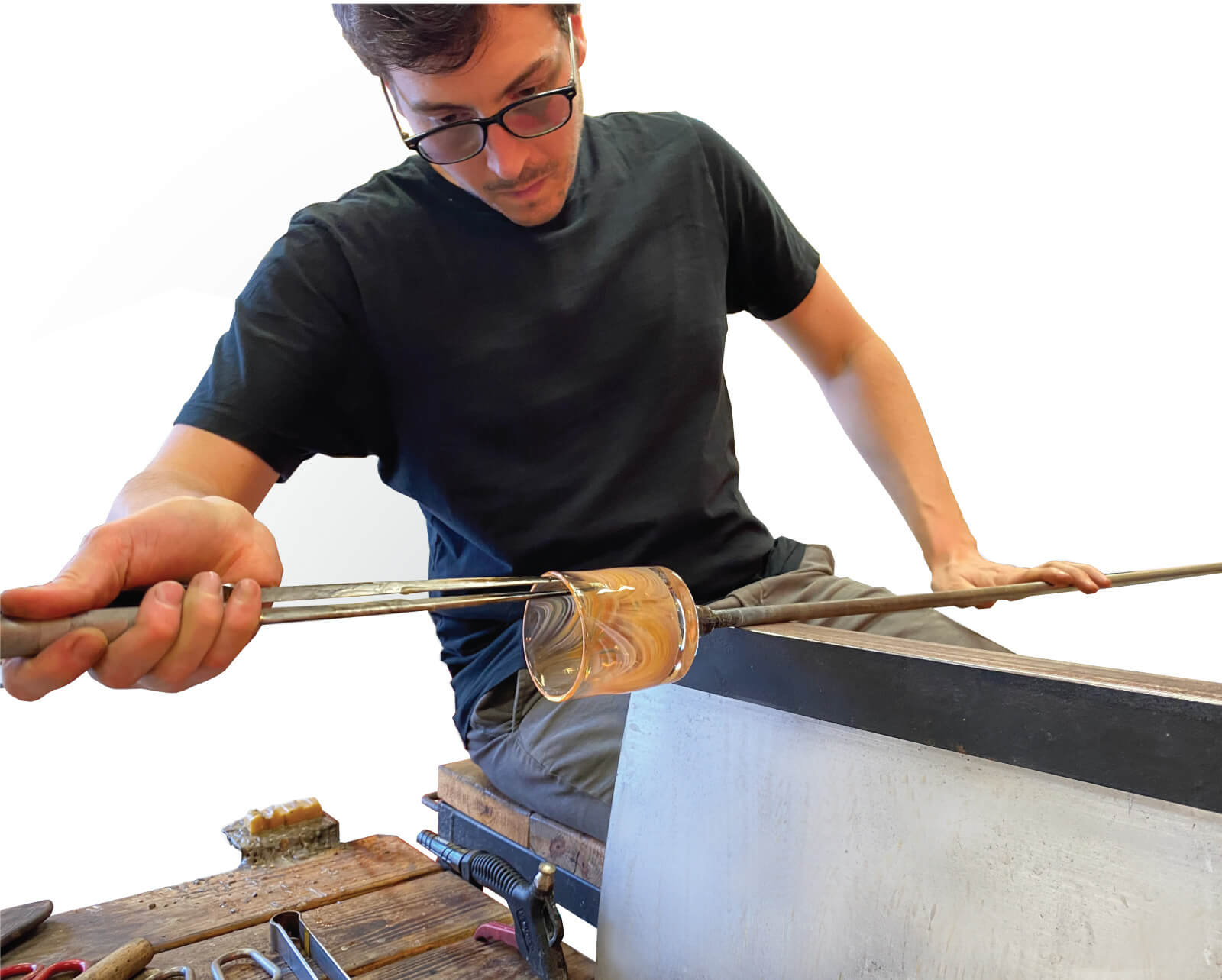 Person with glasses working on glassblowing, shaping molten glass with a blowpipe, wearing a black shirt.